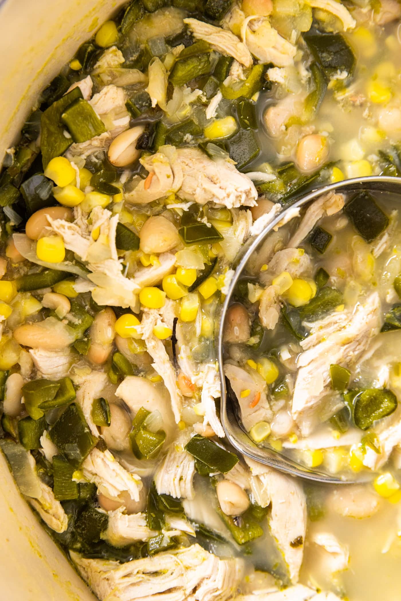 Top down view of interior of large Dutch oven filled with white bean chicken chili with pieces of sweet corn, peppers, and shredded chicken