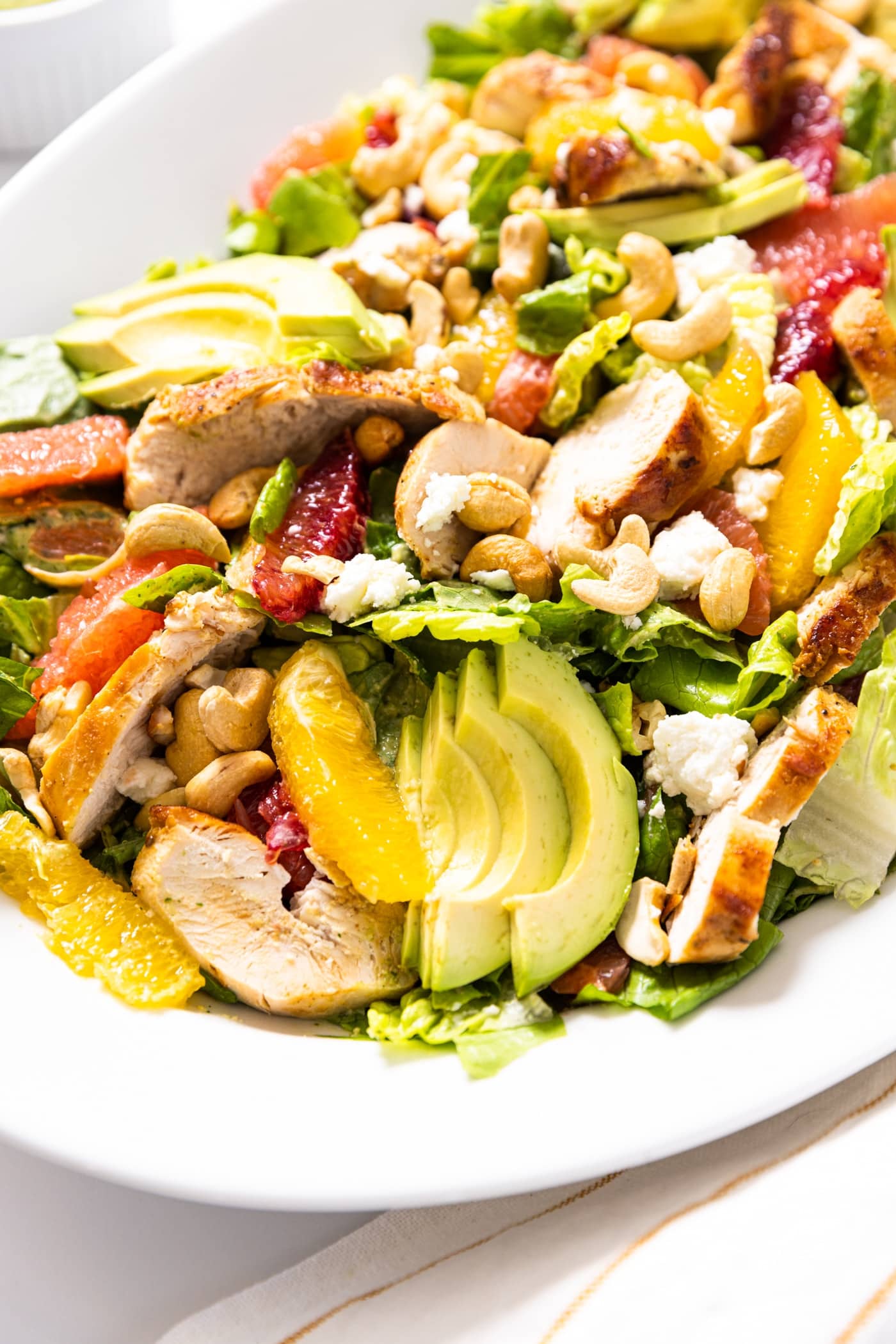 White serving platter sitting on white countertop piled with greens topped with green dressing along with chicken and pieces of citrus and avocado