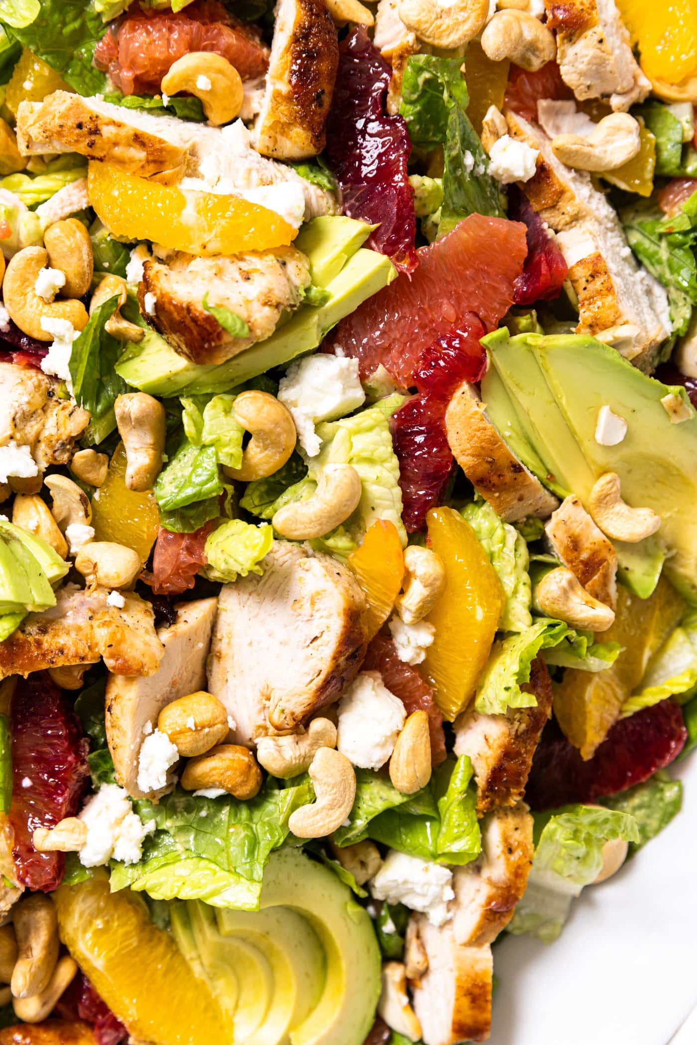 Top down view of citrus chicken salad sitting in white bowl filled with pieces of citrus and green dressing