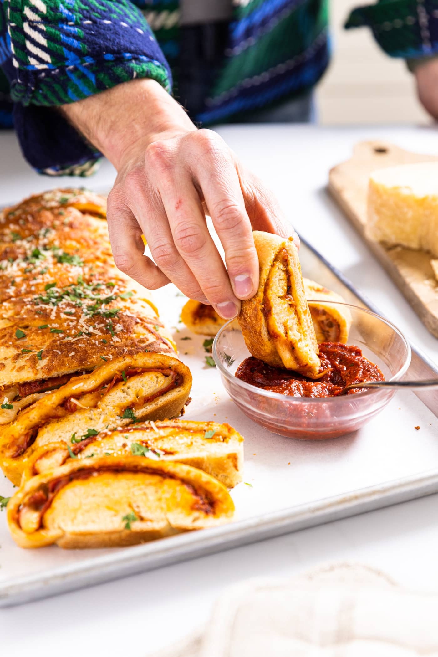 Hand dipping slice of stromboli into red tomato sauce sitting in small glass bowl with rest of stromboli sitting beside