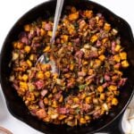 Top down view of black skillet sitting on white countertop filled with corned beef sweet potato has with dill sprinkled over the top with spoon sitting in middle
