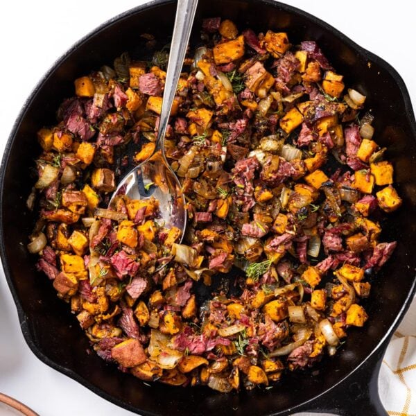 Top down view of black skillet sitting on white countertop filled with corned beef sweet potato has with dill sprinkled over the top with spoon sitting in middle