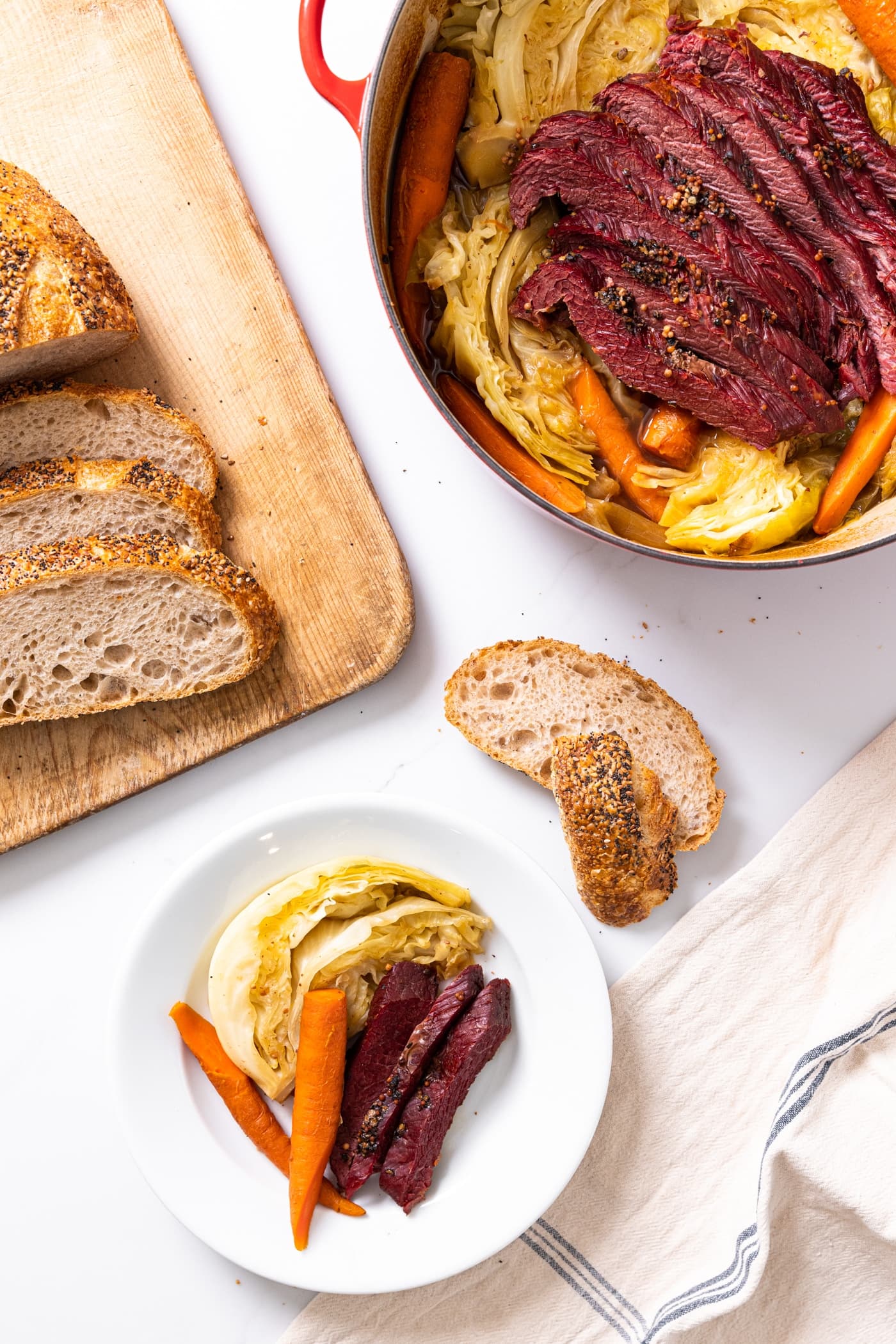 White plate filled with serving of red colored corned beef with cabbage and carrots and large Dutch oven filled with rest of corned beef all on white countertop