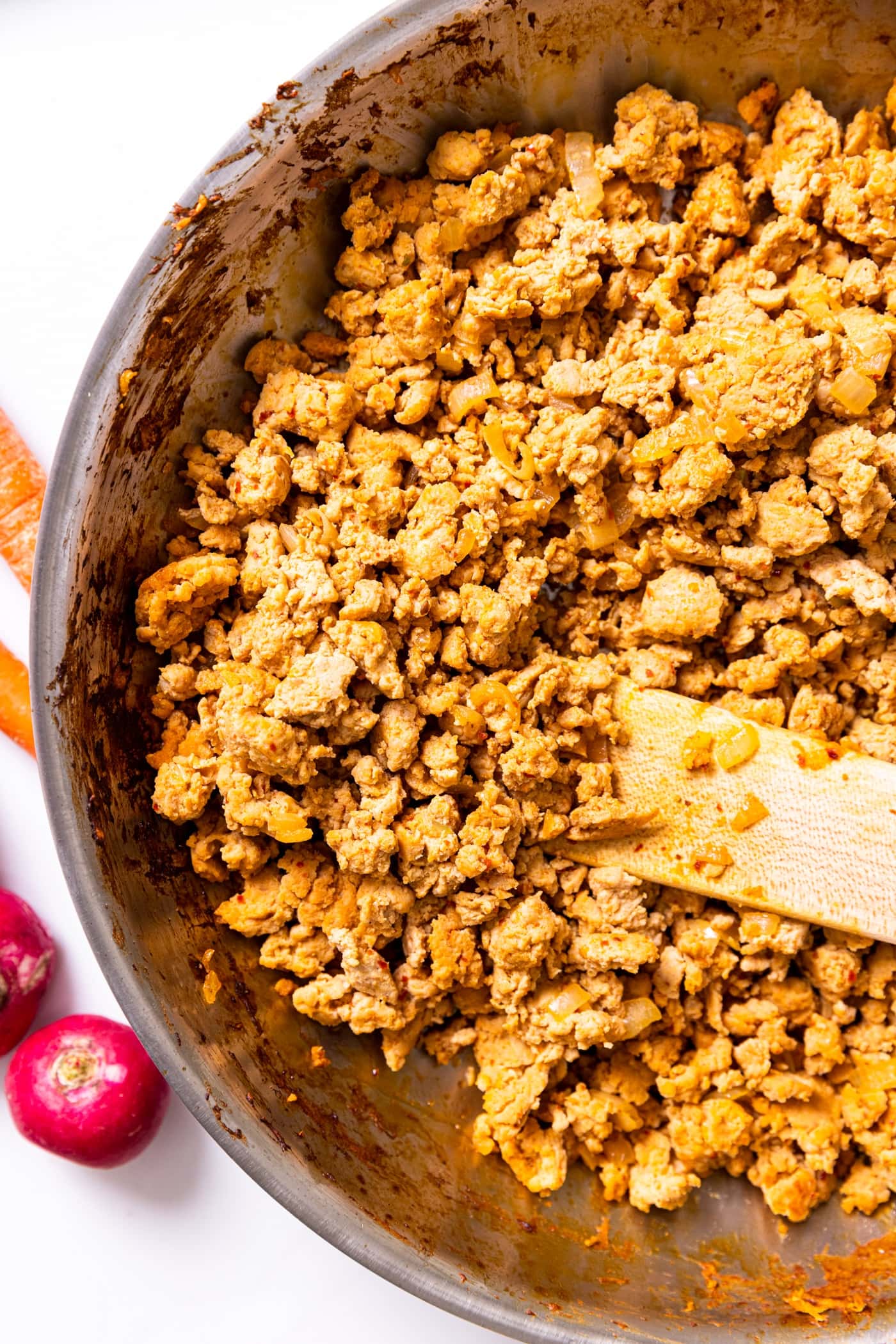 Top down view of skillet filled with spicy chicken sitting on white countertop with wood spatula sitting amidst the meat