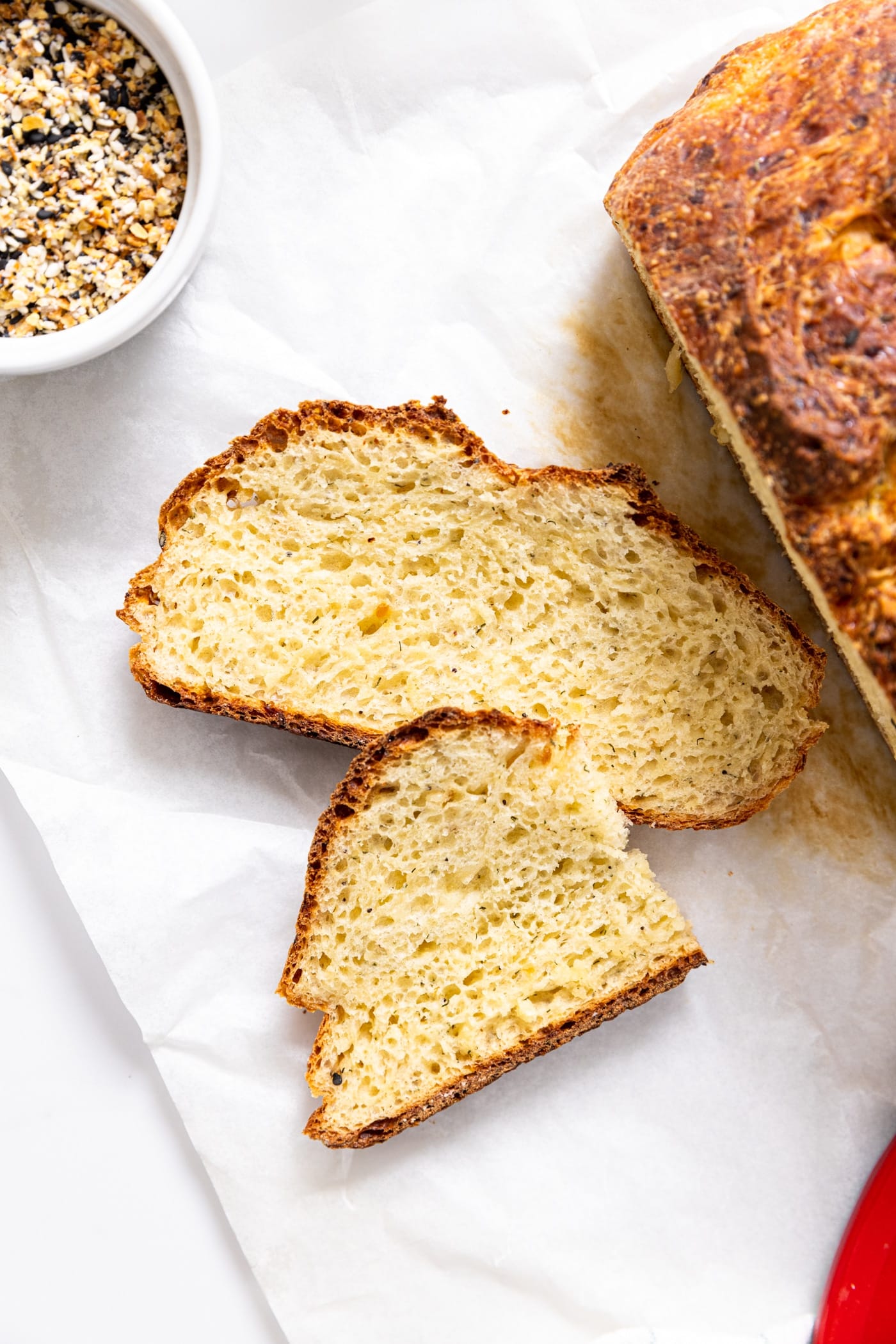 Two slices of dilly bread sitting on piece of white parchment on countertop with rest of loaf sitting beside