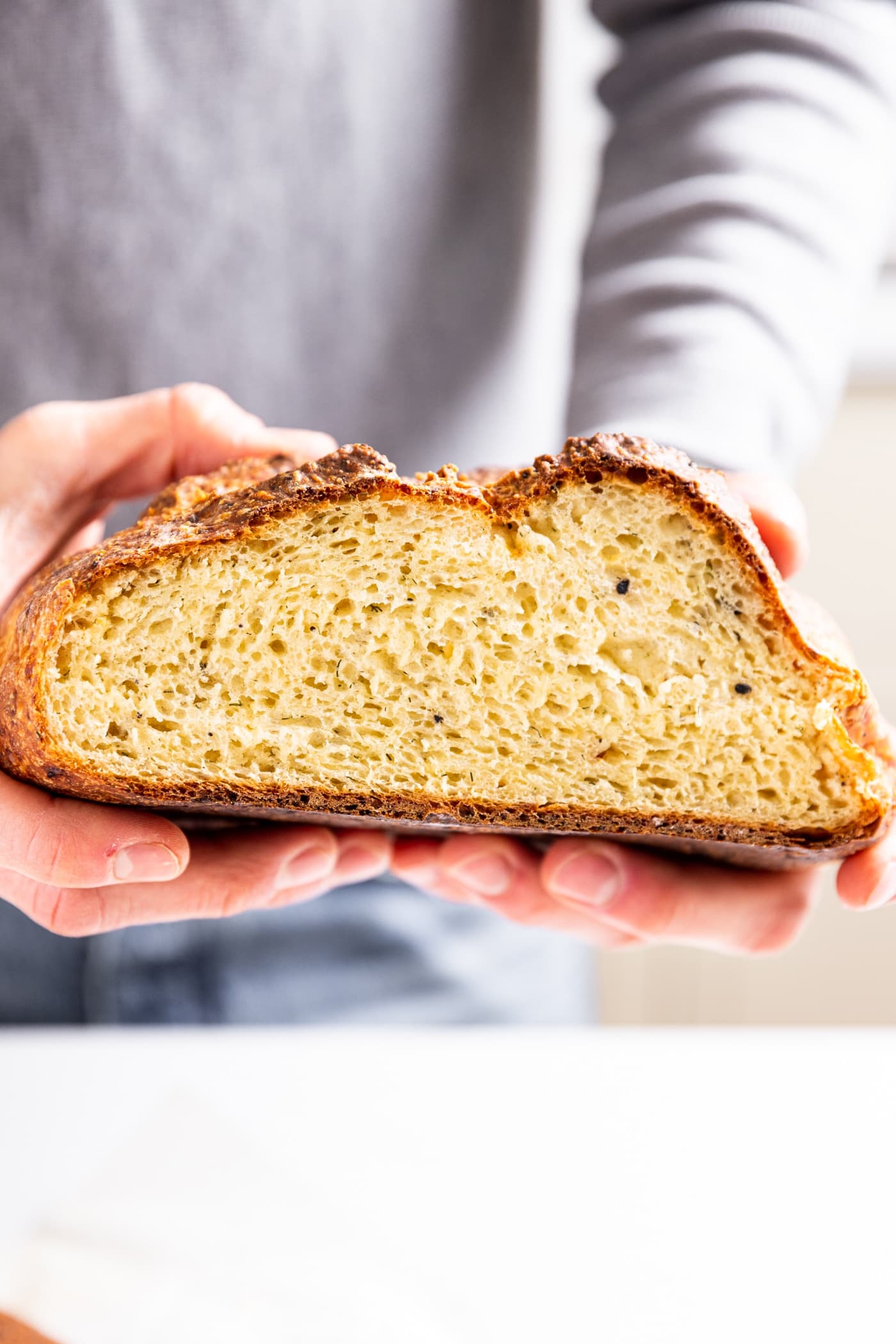 Loaf of bread being held by two hands with end sliced off showing golden interior of dilly bread