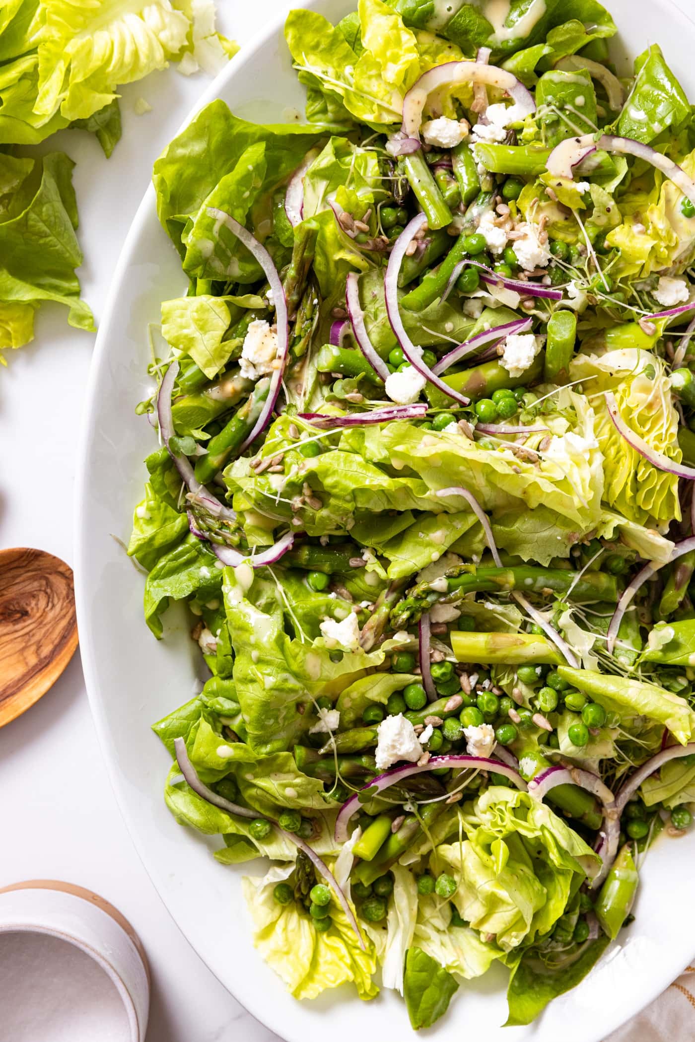 Top down view of white serving platter filled with buttercrunch lettuce topped with red onion and goat cheese with wooden tongs sitting on countertop