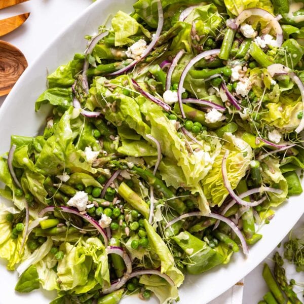 Top down view of white serving platter filled with lettuce topped with slices of red onion and topped with goat cheese with wood tongs sitting on countertop