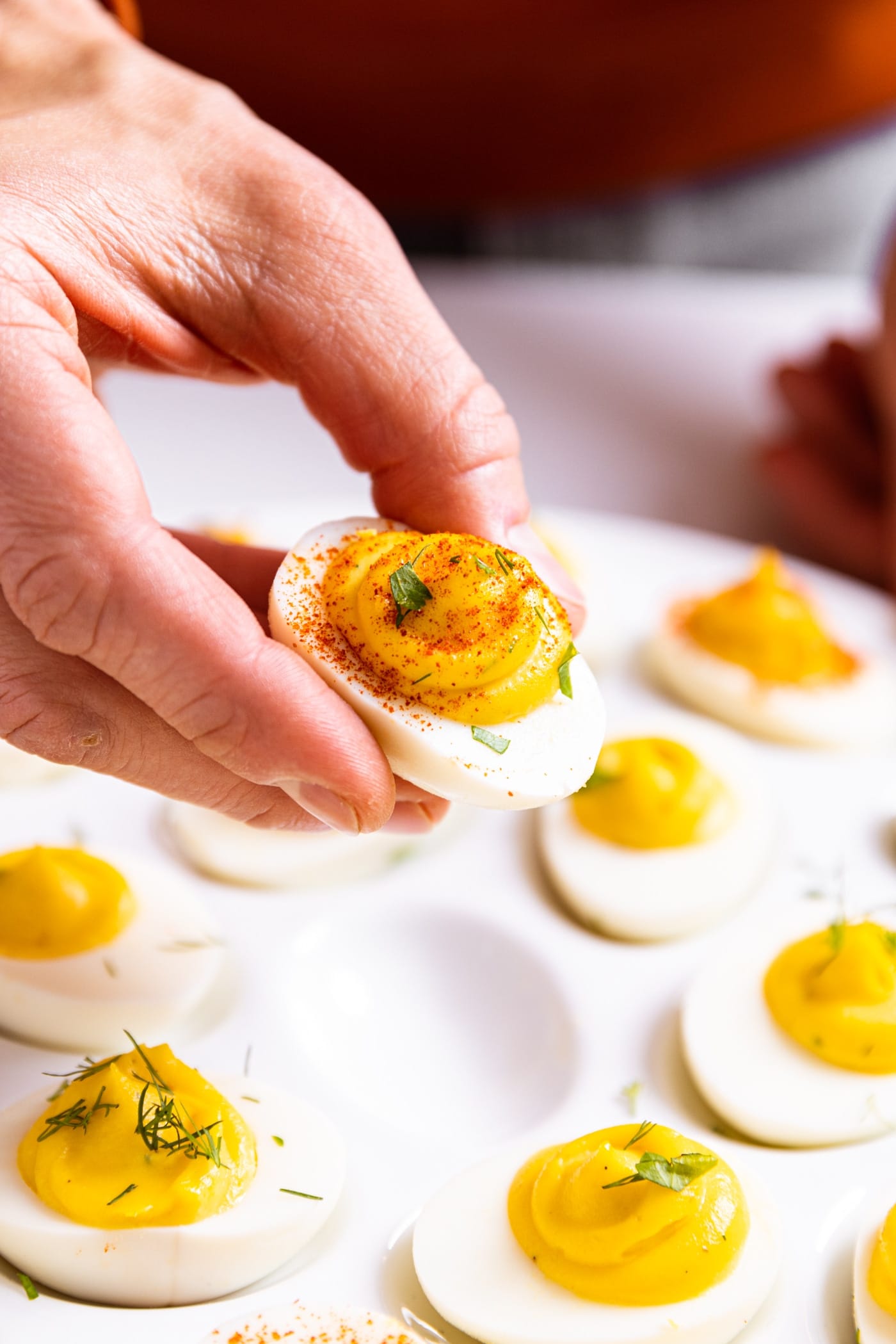 Hand holding half of white deviled egg filled with yellow colored creamy texture and topped with paprika powder