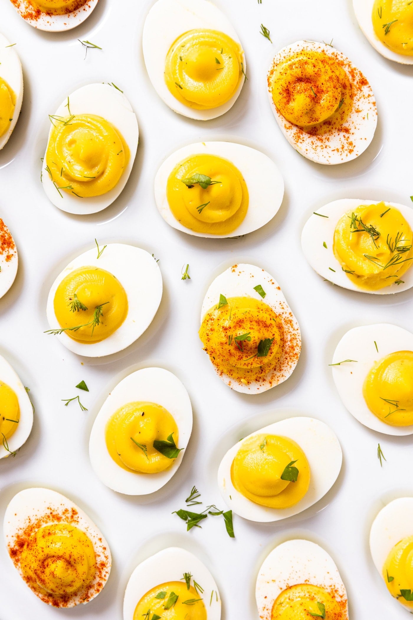 Top down view of white plate filled with halves of white eggs filled with creamy yellow filling and topped with dill and paprika