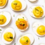 Top down view of white plate filled with deviled eggs filled with yellow colored creamy filling and topped with paprika and dill