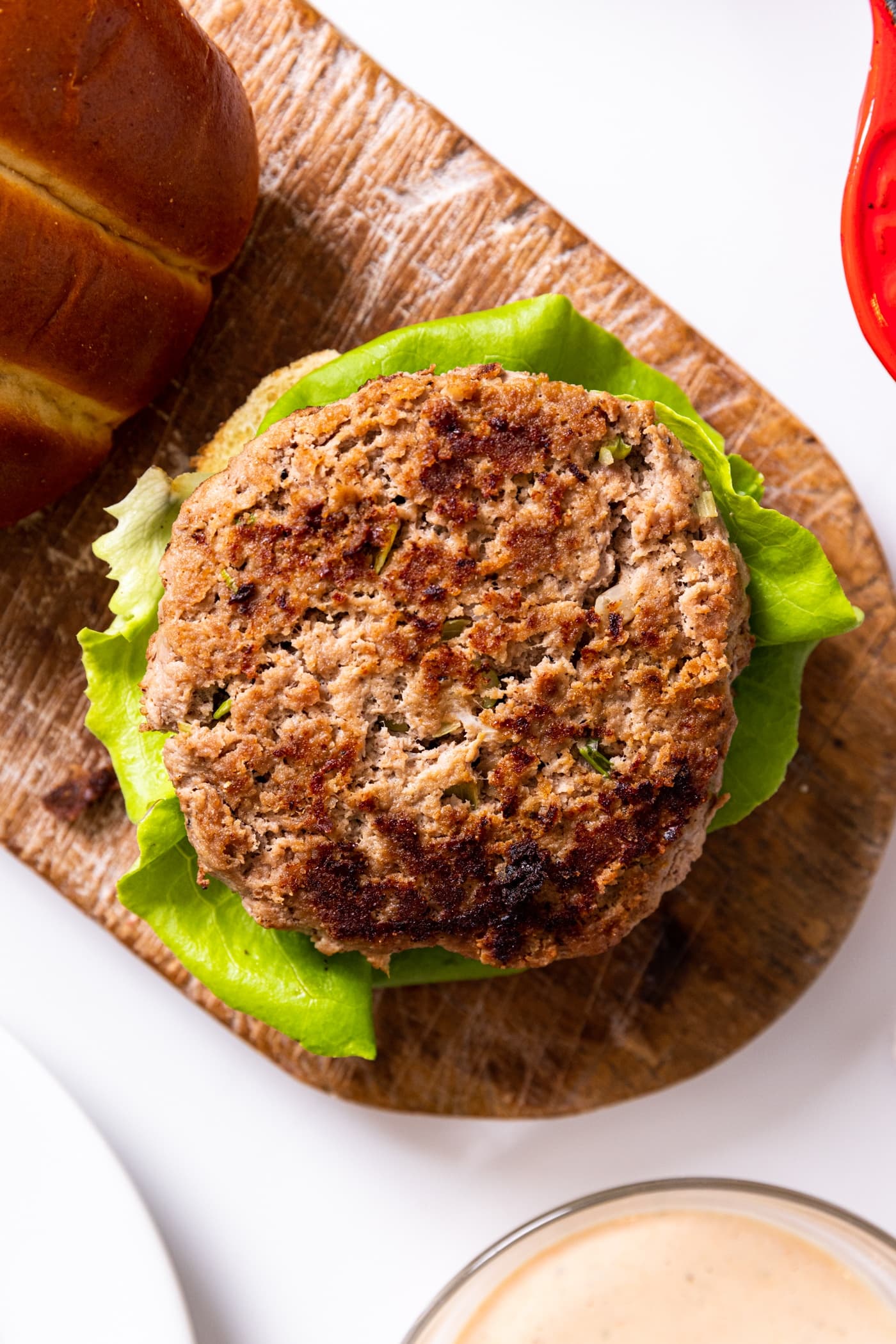 Top down view of turkey burger sitting on bun with slice of lettuce all on white countertop with glass bowl filled with white colored sauce