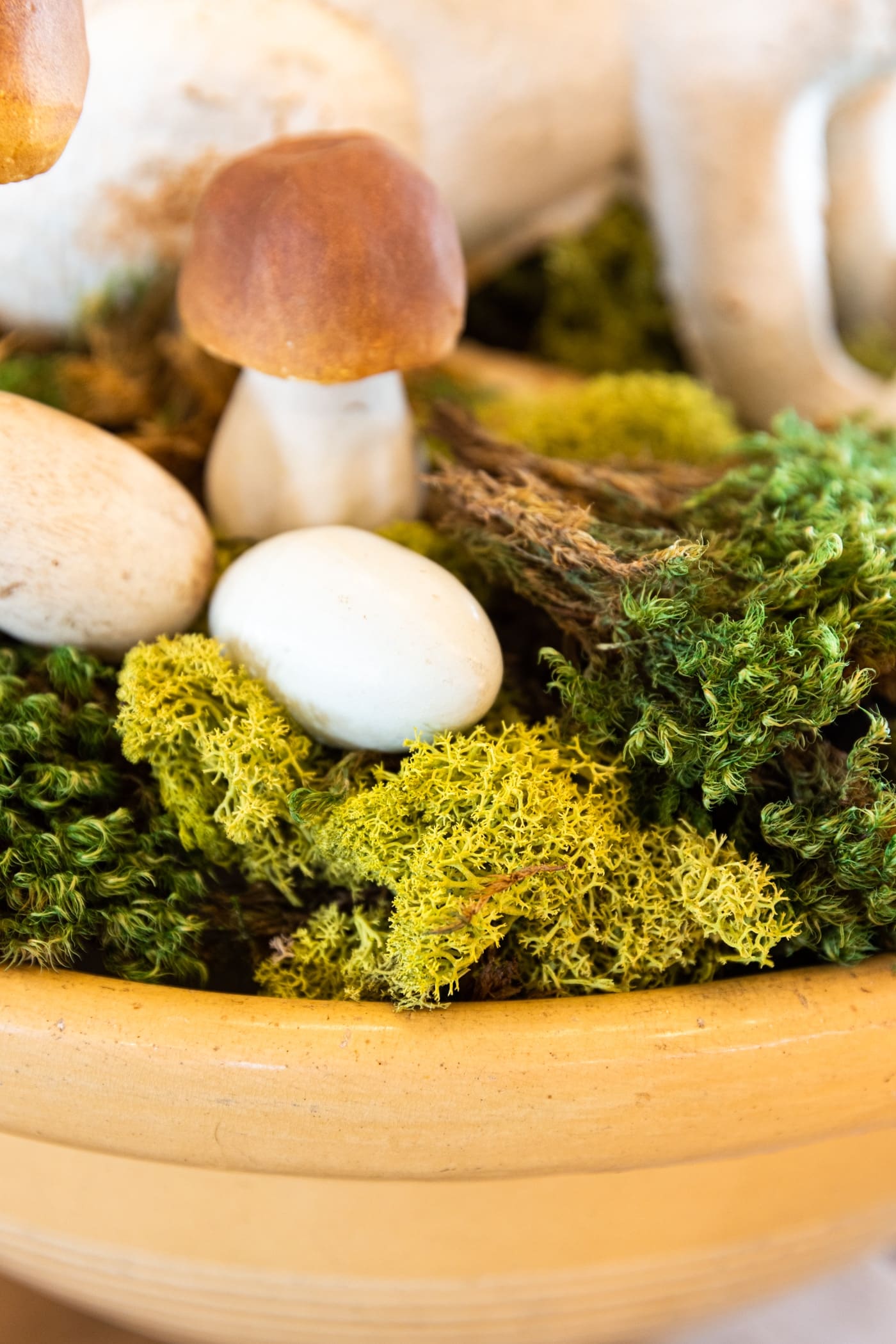 Large yellow bowl filled with green moss with white preserved eggs sitting among the moss with metal rabbit on top