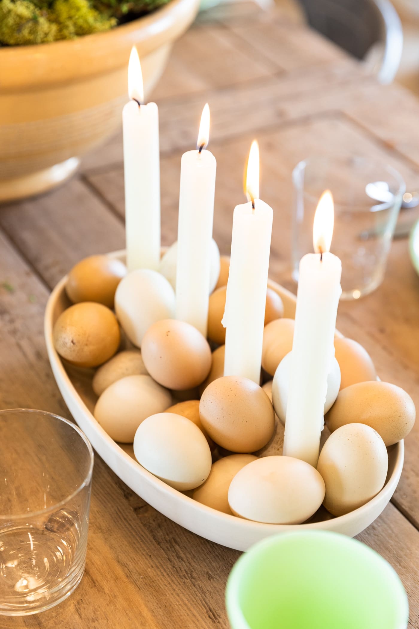 Oval white bowl filled with candles on fire with light white and taupe colored preserved eggs all on wood dining table
