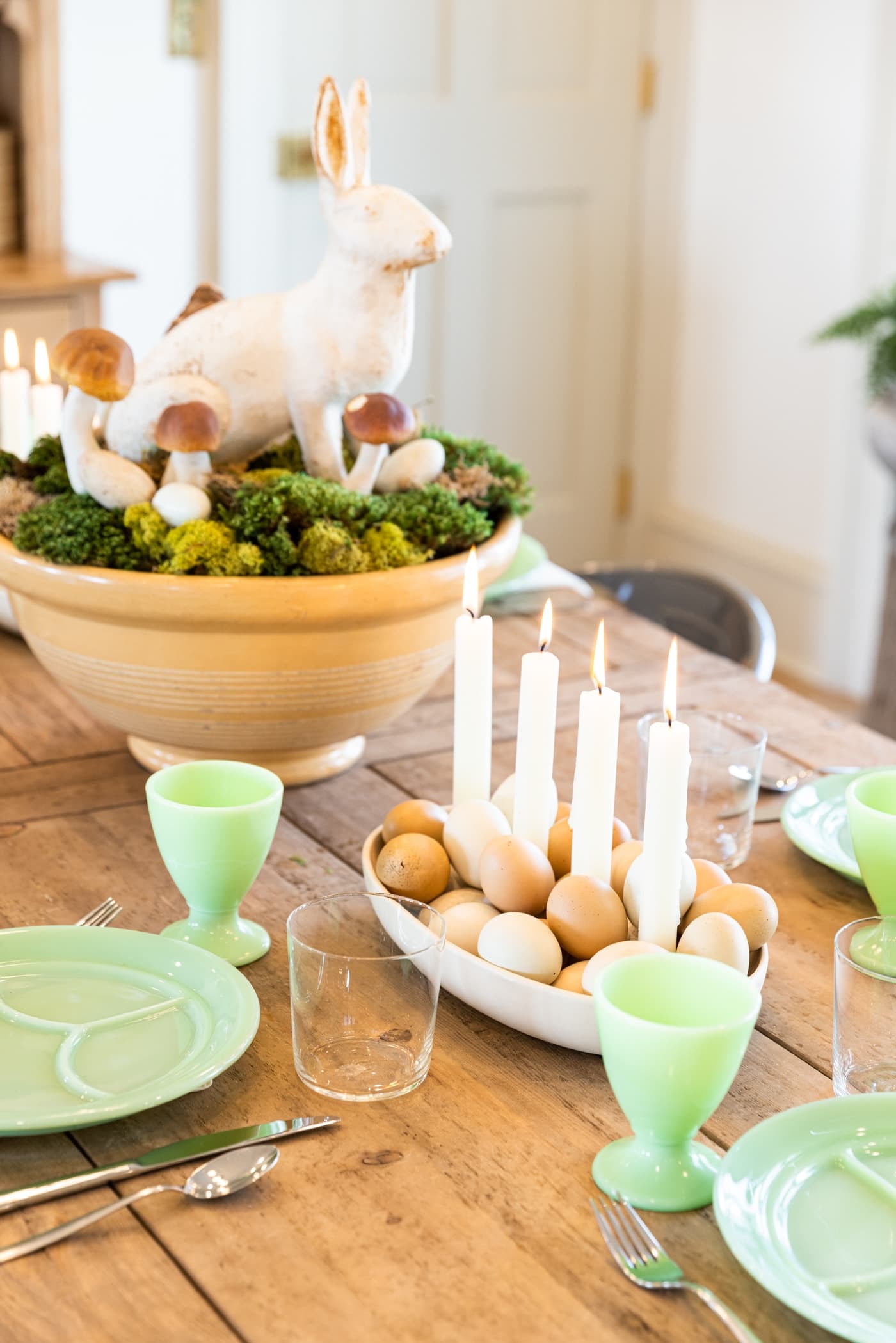 Large spring centerpiece in yellow bowl sitting on wood dining table set with jadeite plates