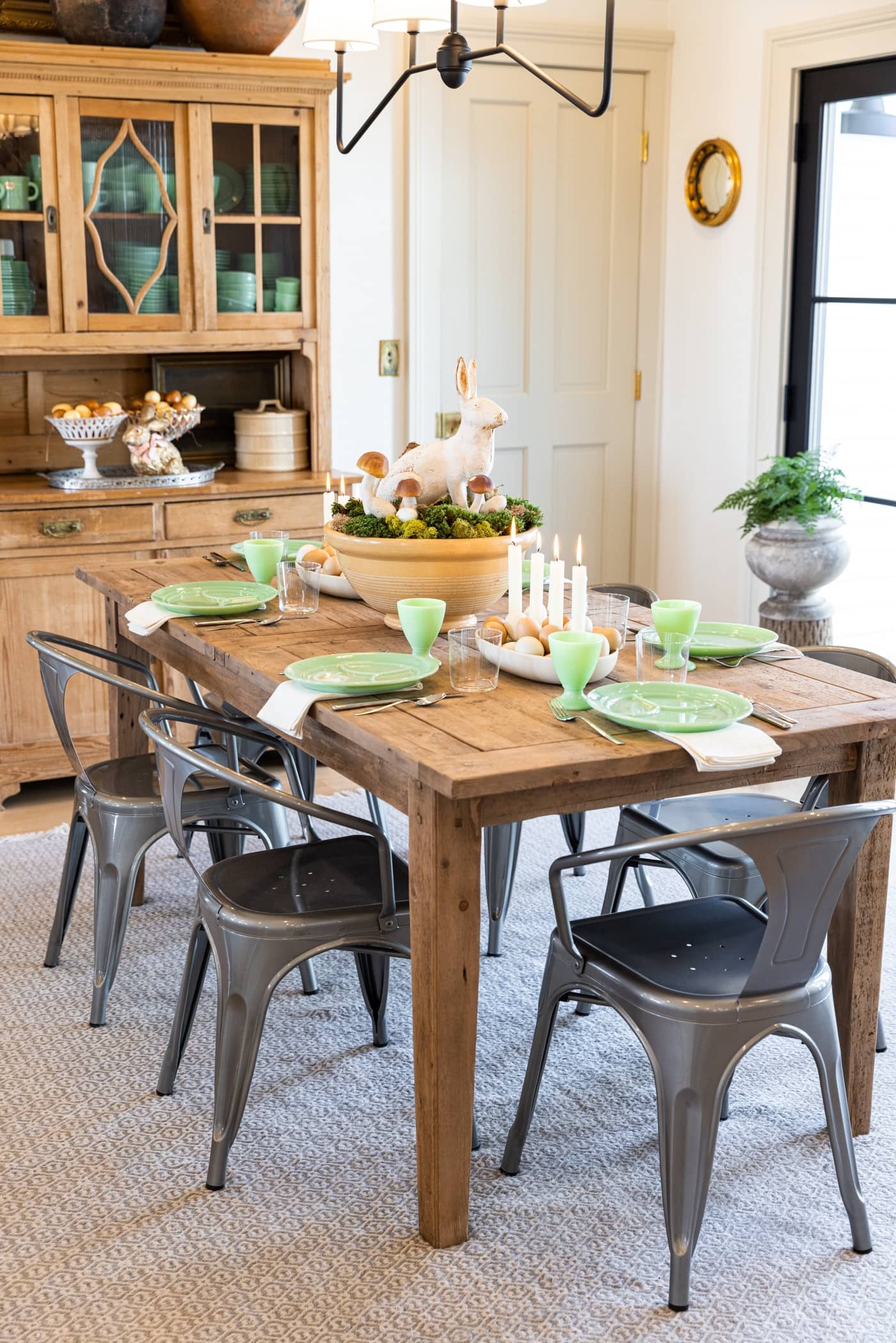 Wood dining table with metal chairs all around set with an Easter centerpiece made with metal rabbit, moss, and eggs