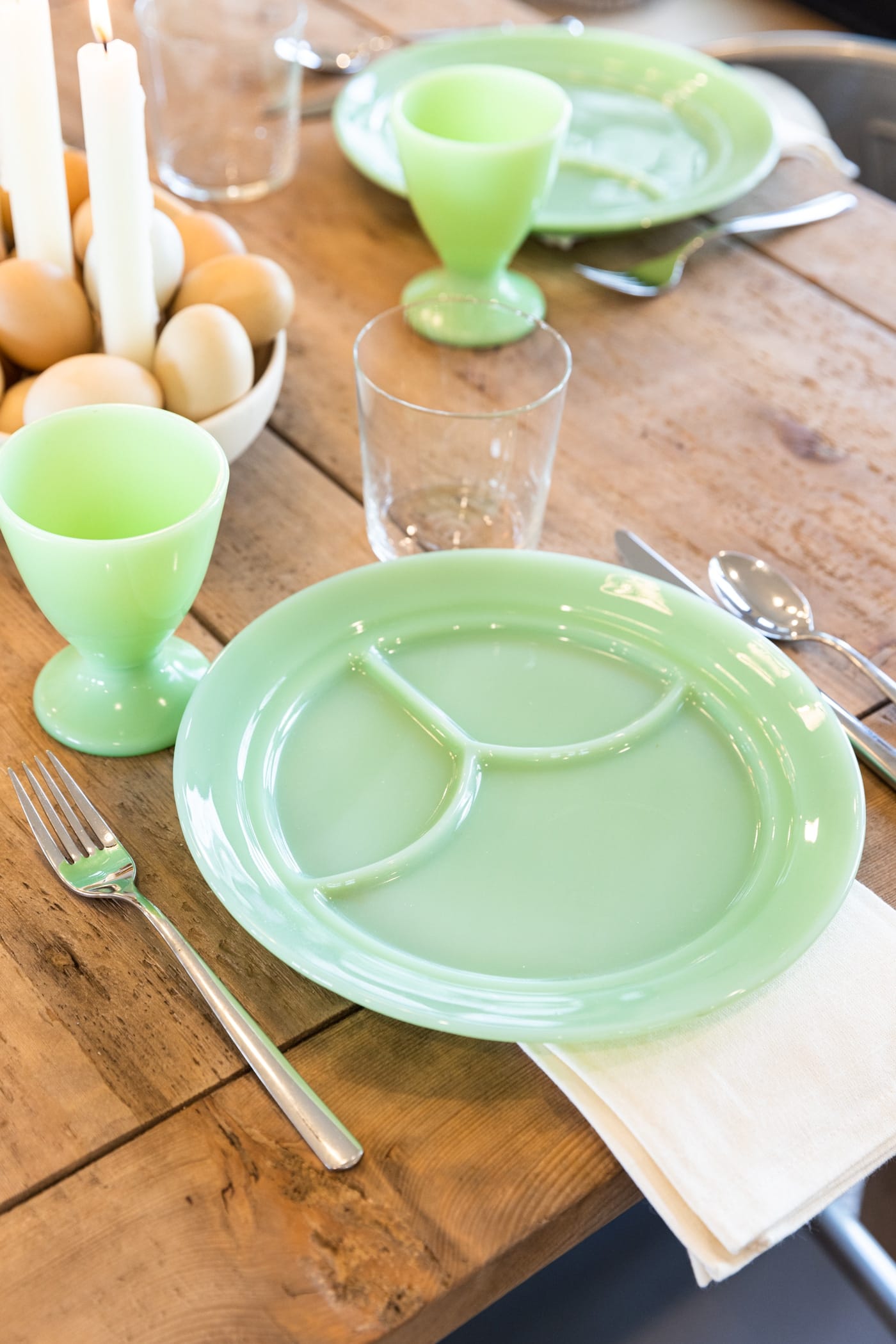 Jadeite plate with white napkin underneath with fork, knife, and spoon all on wood dining table