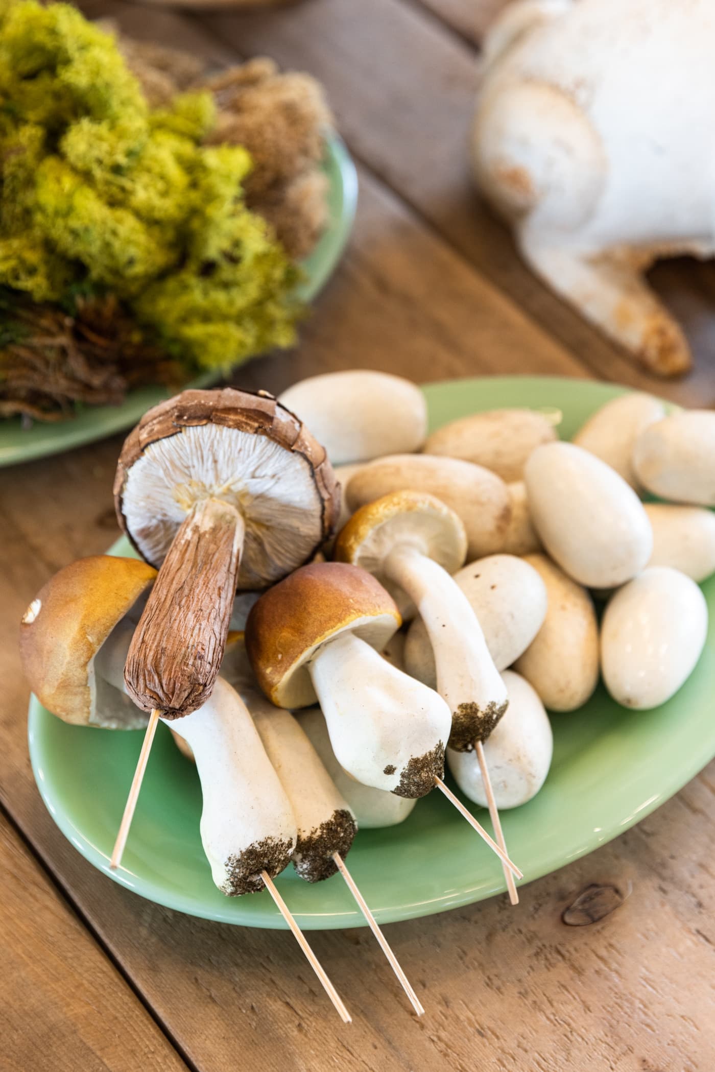 Jadeite plate filled with faux mushrooms of all different colors and sizes sitting on wood dining table