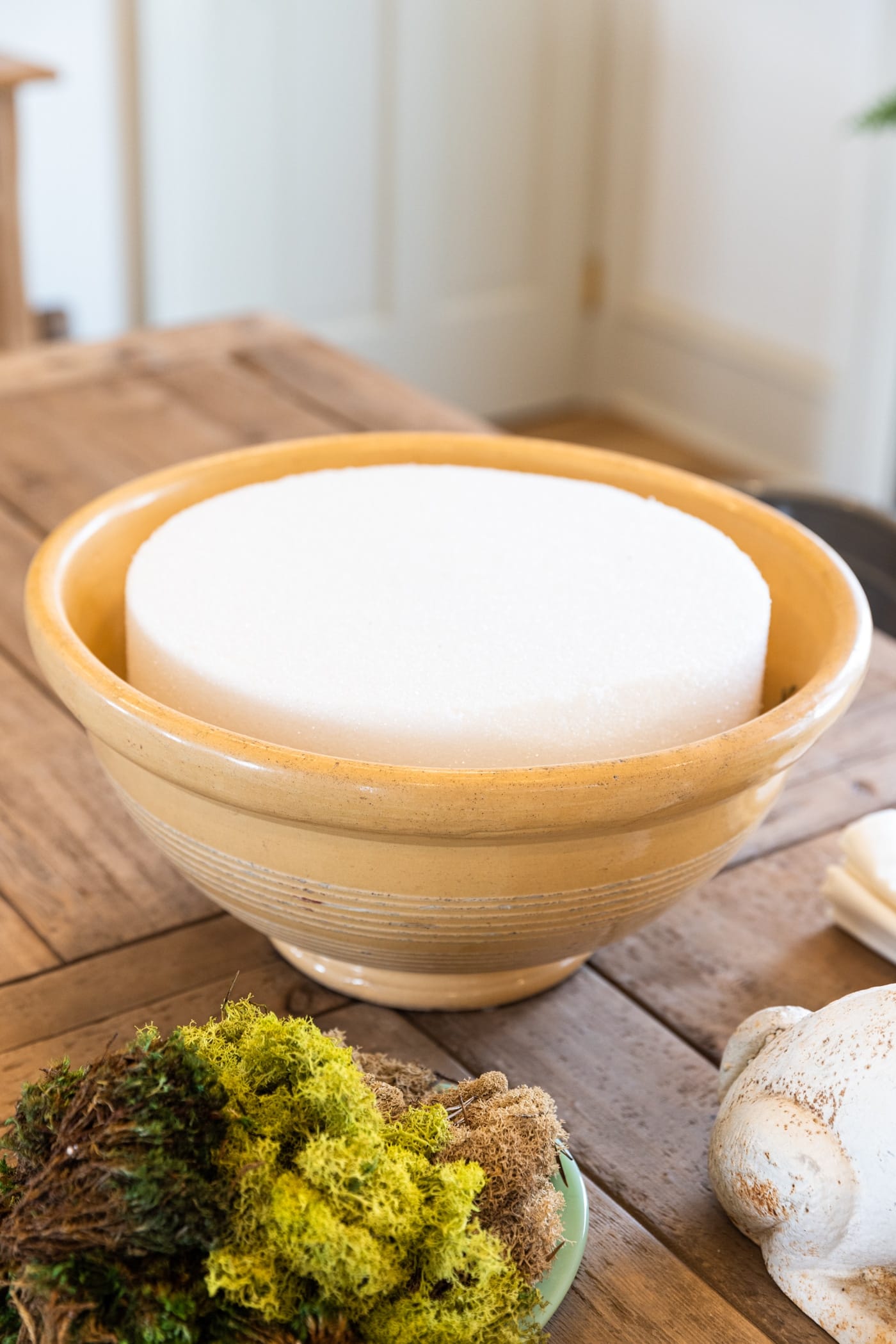 Large yellowware bowl with piece of styrofoam in the middle sitting on wood dining table