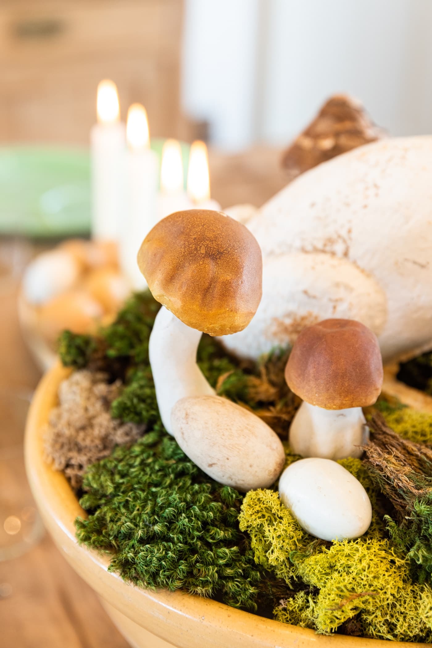 Large curved mushroom sitting among green colored moss with white candles in background all on dining table