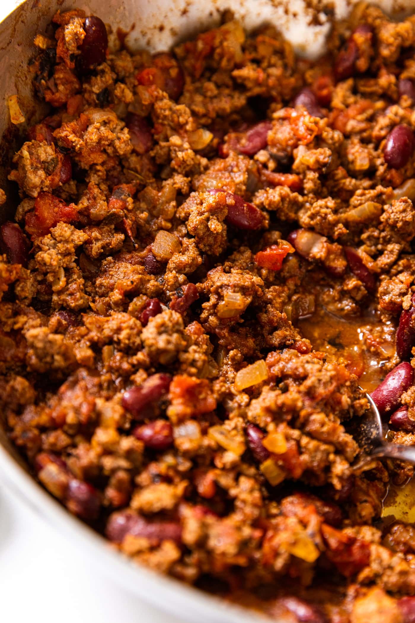 Meat mixture made of ground beef and kidney beans sitting in metal bowl with spoon inside