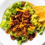 Top down view of white plate sitting on countertop filled with large taco salad with guacamole and chips on the side