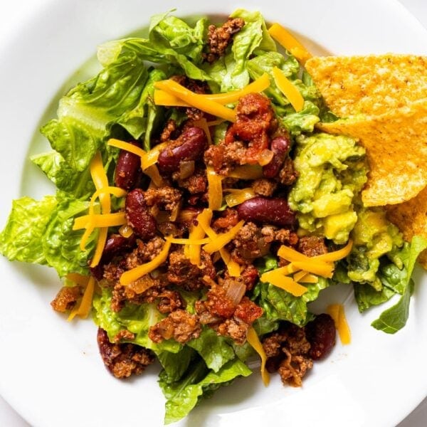 Top down view of white plate sitting on countertop filled with large taco salad with guacamole and chips on the side