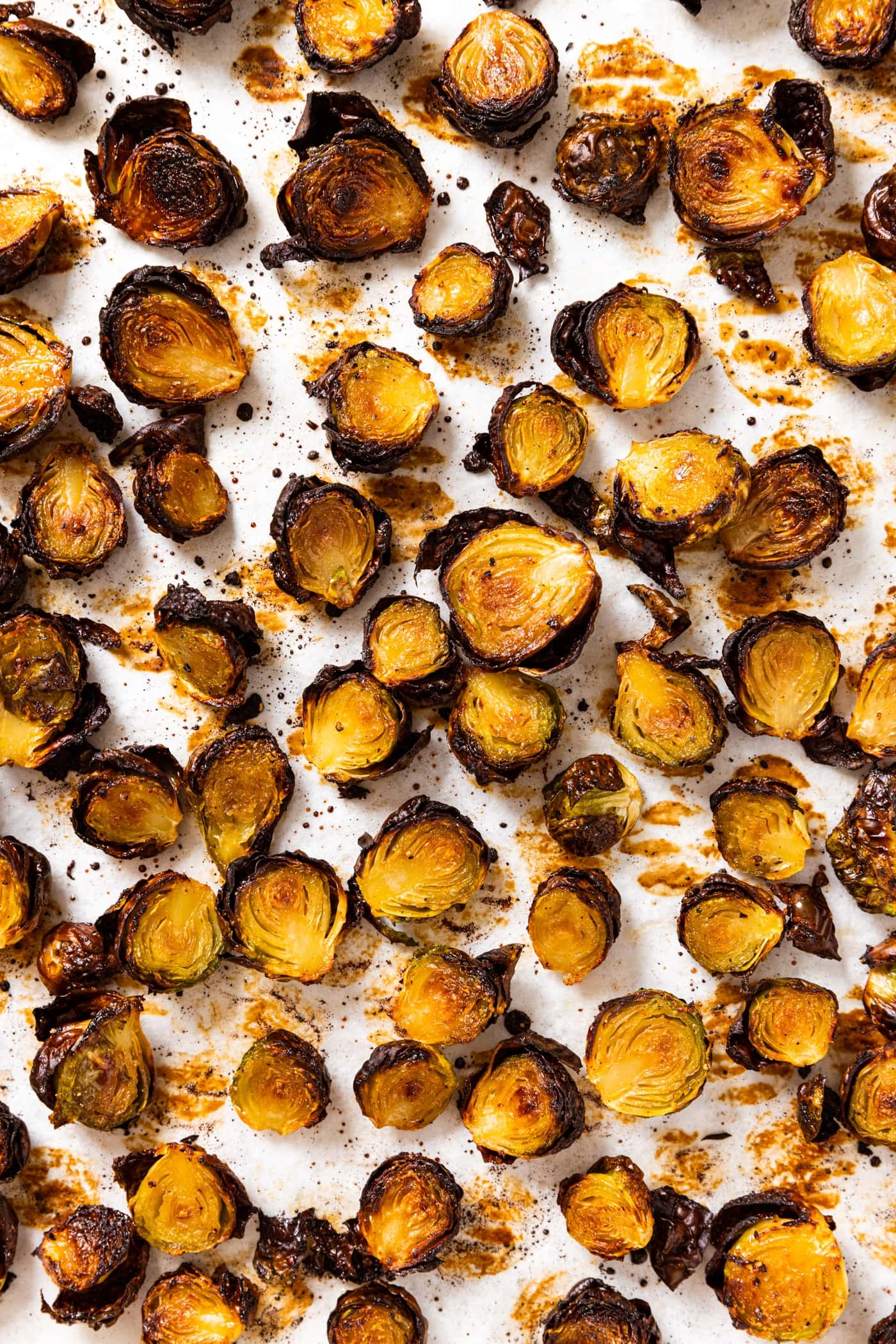 Top down view of lots of crispy Brussels sprouts sitting on parchment-lined baking sheet after coming out of the oven