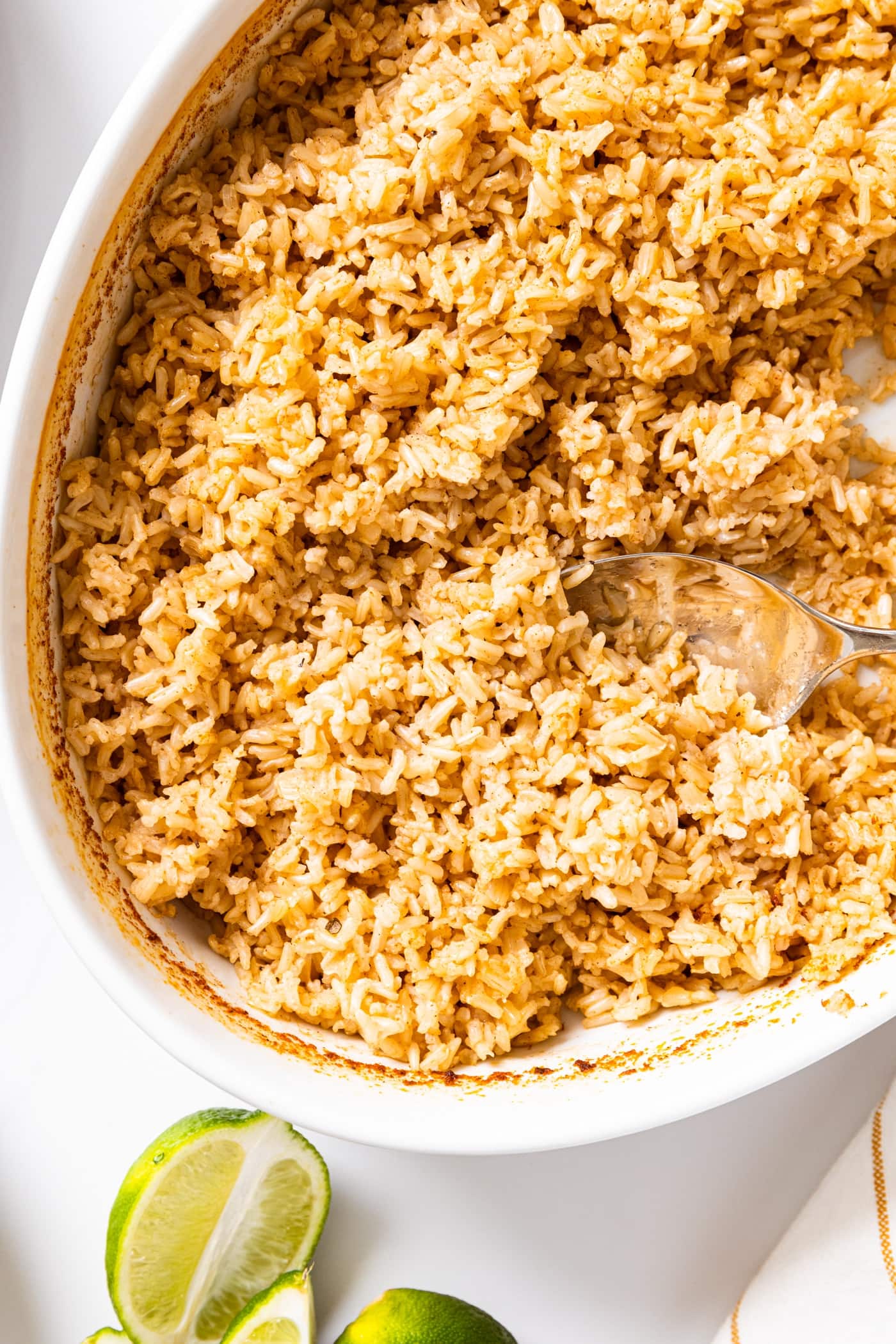 White oval bowl filled with brown rice with spices on top with lime slices as well