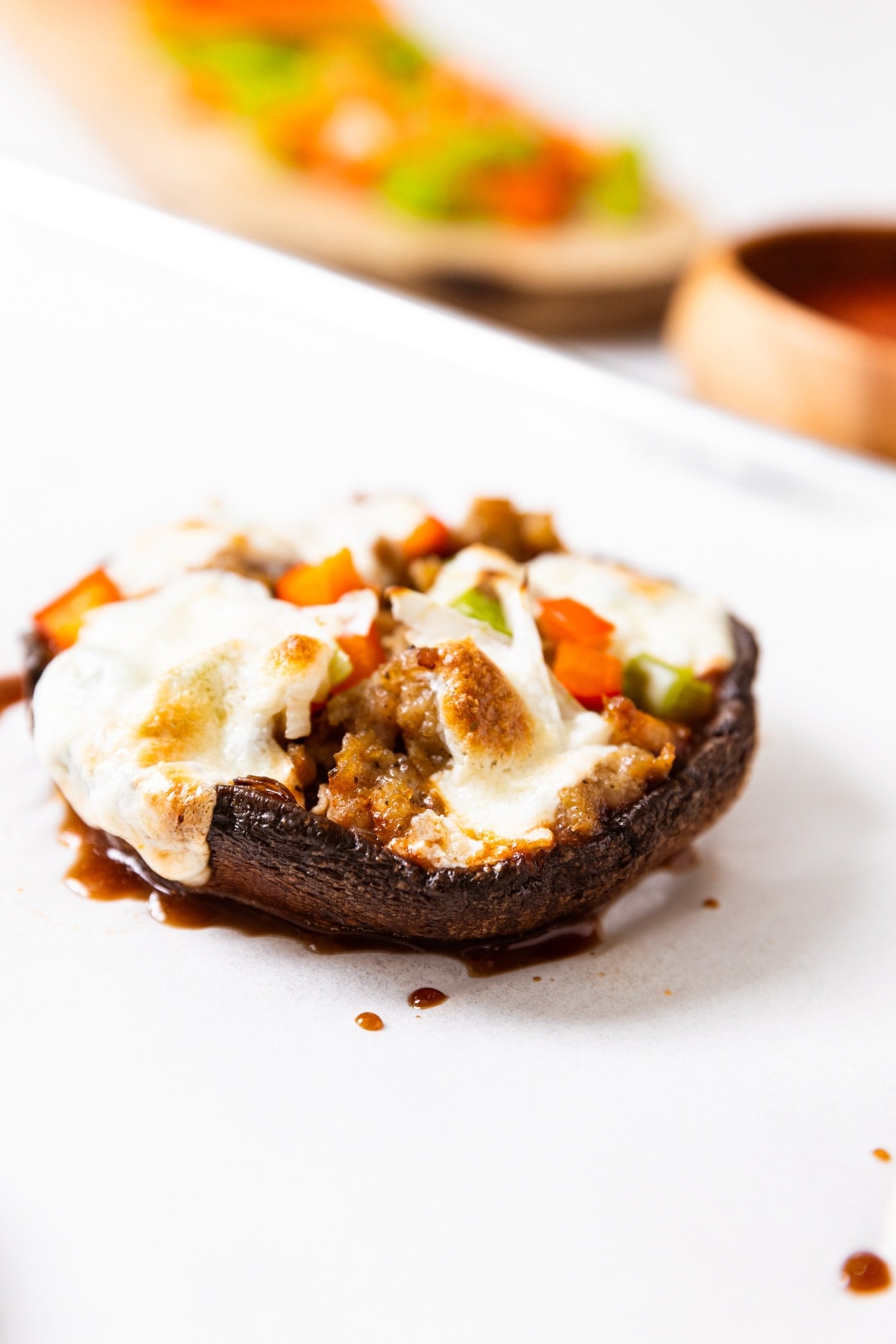 Side view of portobello mushroom that was made into a pizza with cheese, red and green pepper, and sausage on top all sitting on white piece of parchment paper