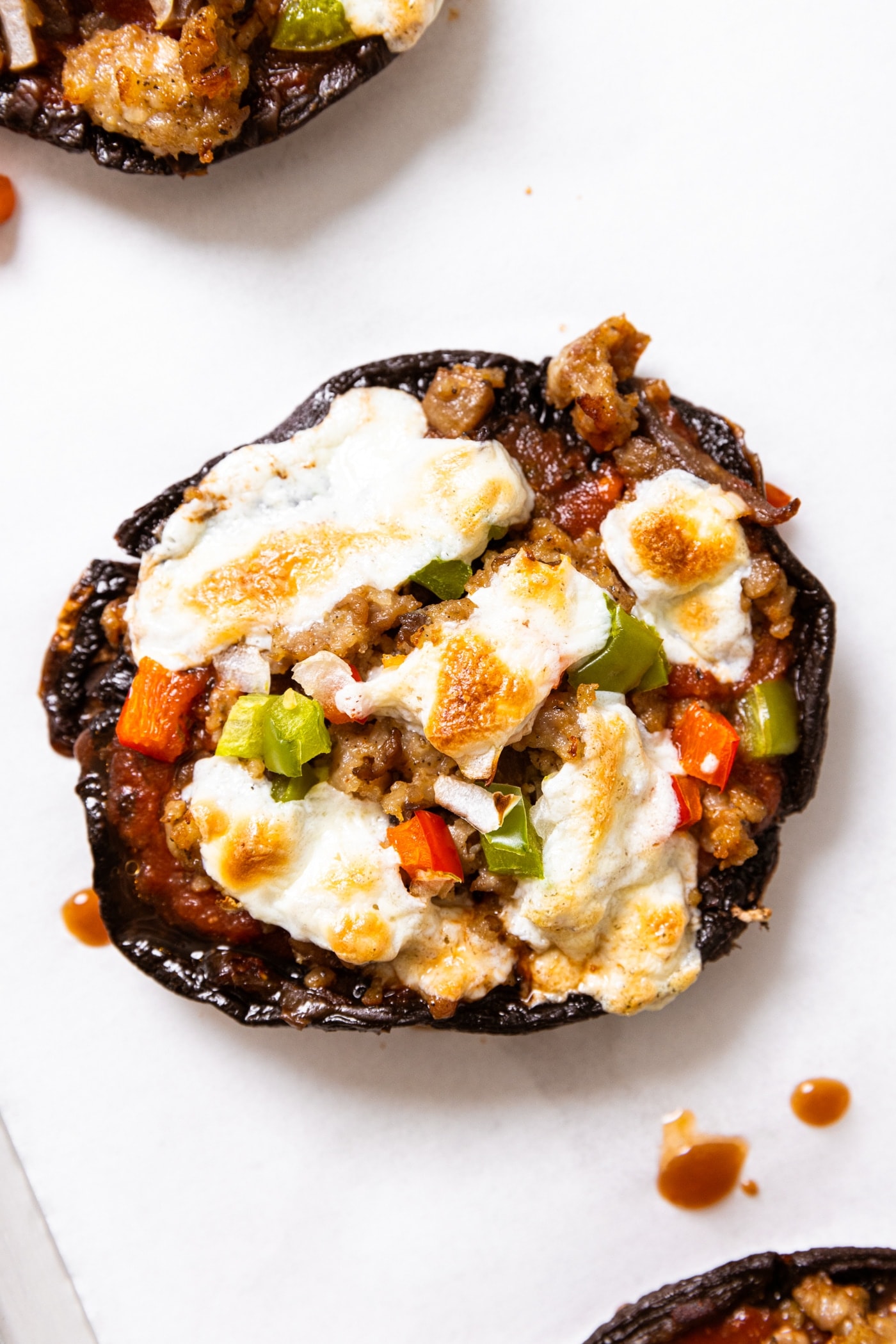 Close up top down view of portobello mushroom pizza with cheese, red and green pepper, and sausage all over the top with other small pizzas around