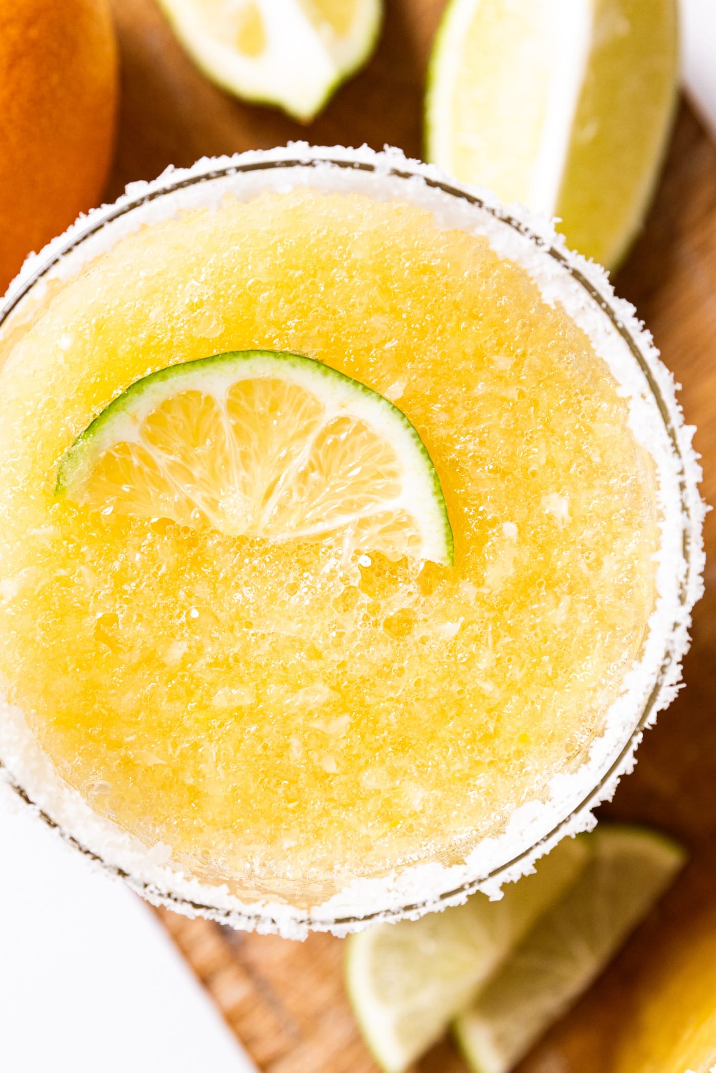 Top down view of glass filled with blended margarita with icy texture showing with glass rim rimmed with salt and lime slice