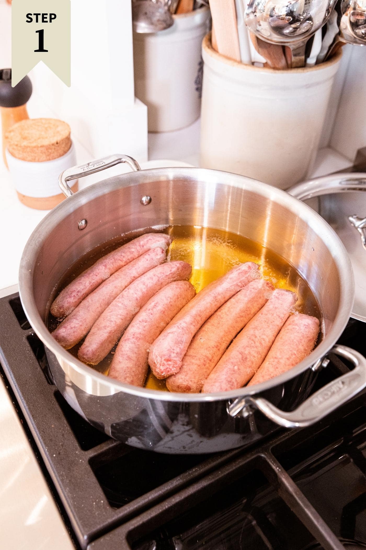 Metal pot sitting on stovetop with uncooked brats in pan with beer liquid all around.