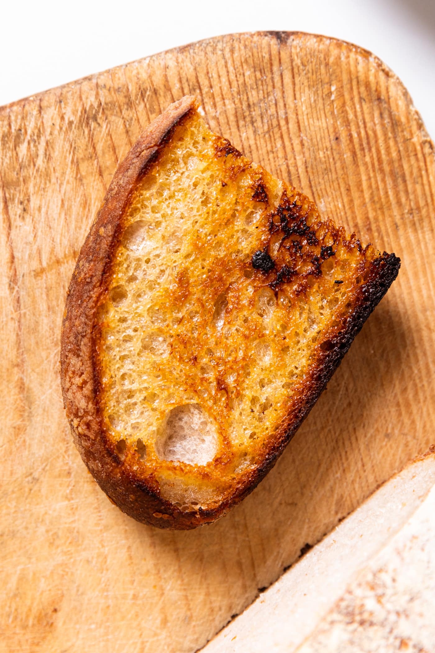 Piece of crusty bread sitting on wood board after being grilled in skillet.