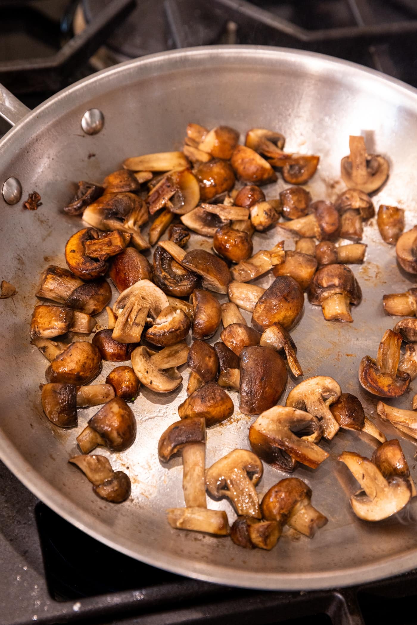 Browned Cremini mushrooms sitting in stainless steel skillet on stove after being cooked.