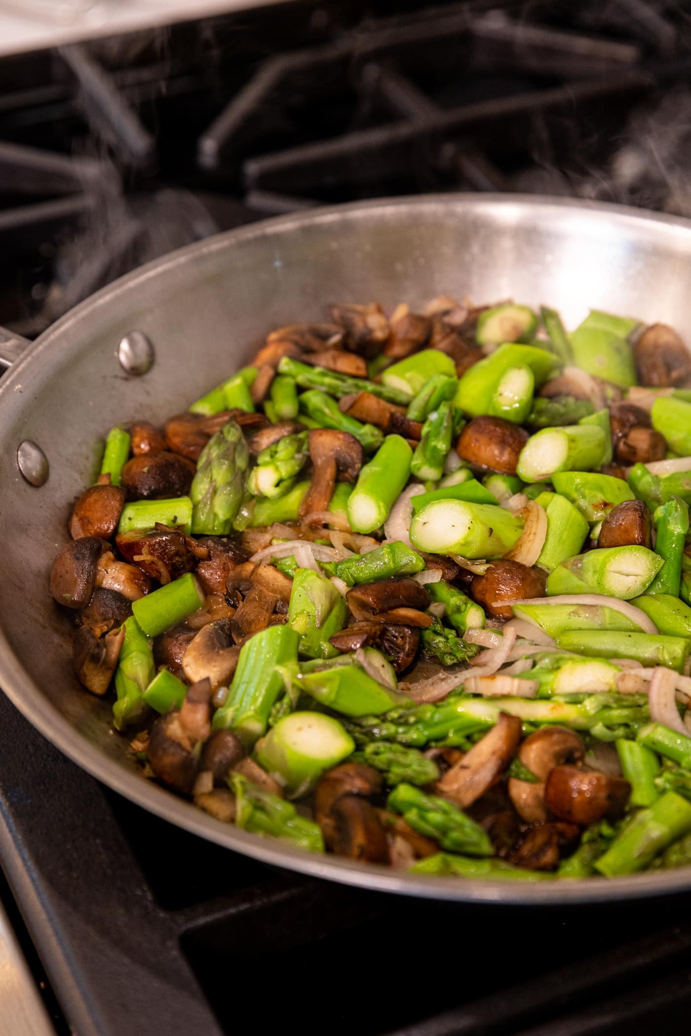 Browned mushrooms and asparagus sitting in stainless steel skillet on stovetop.