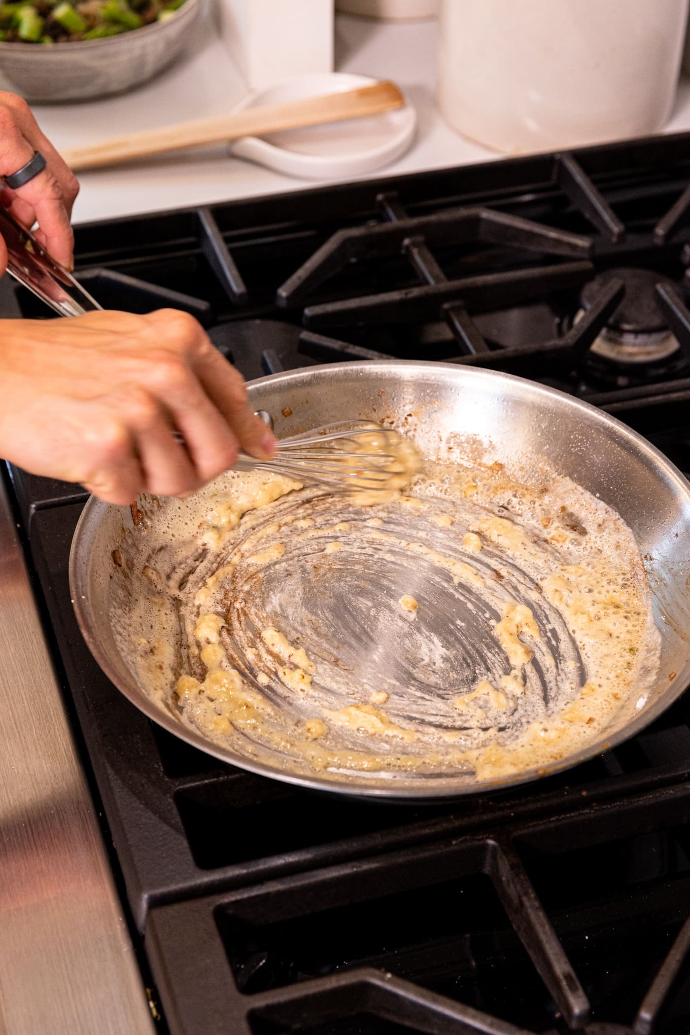 Hand whisking roux sauce in skillet on stovetop.