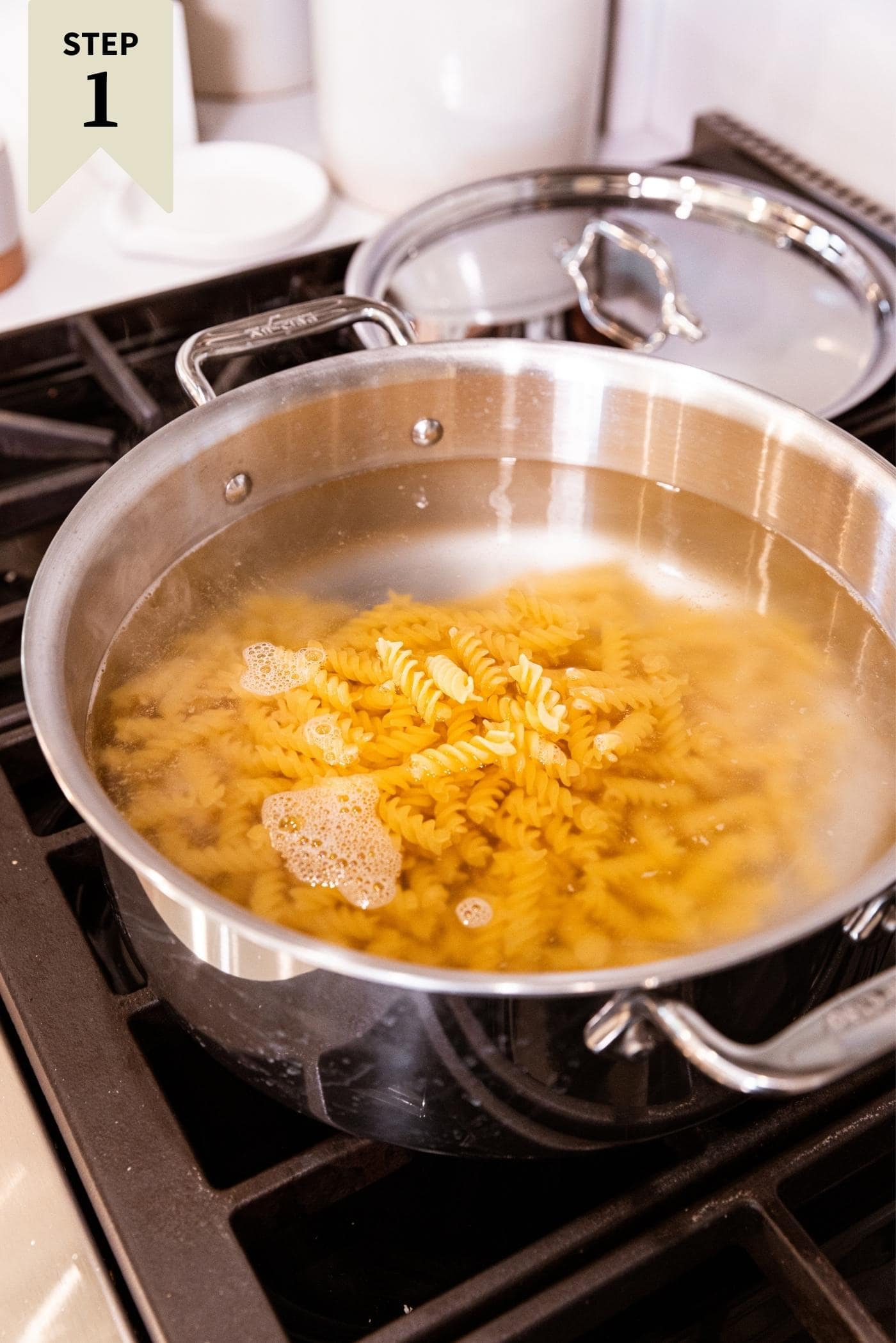 Large steel pot sitting on stovetop filled with water with yellow colored spiral pasta sitting in water.