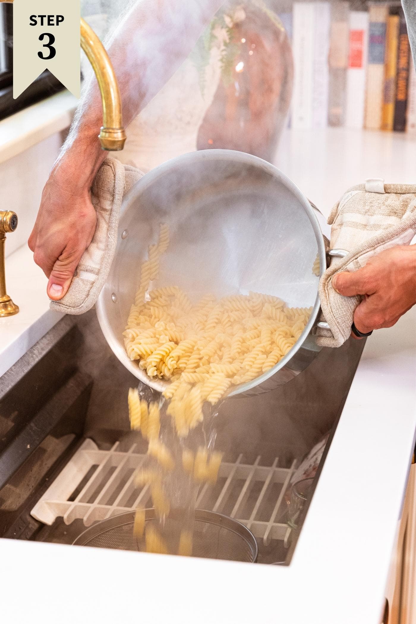 Two hands holding steel pot draining the water from freshly cooked spiral pasta.