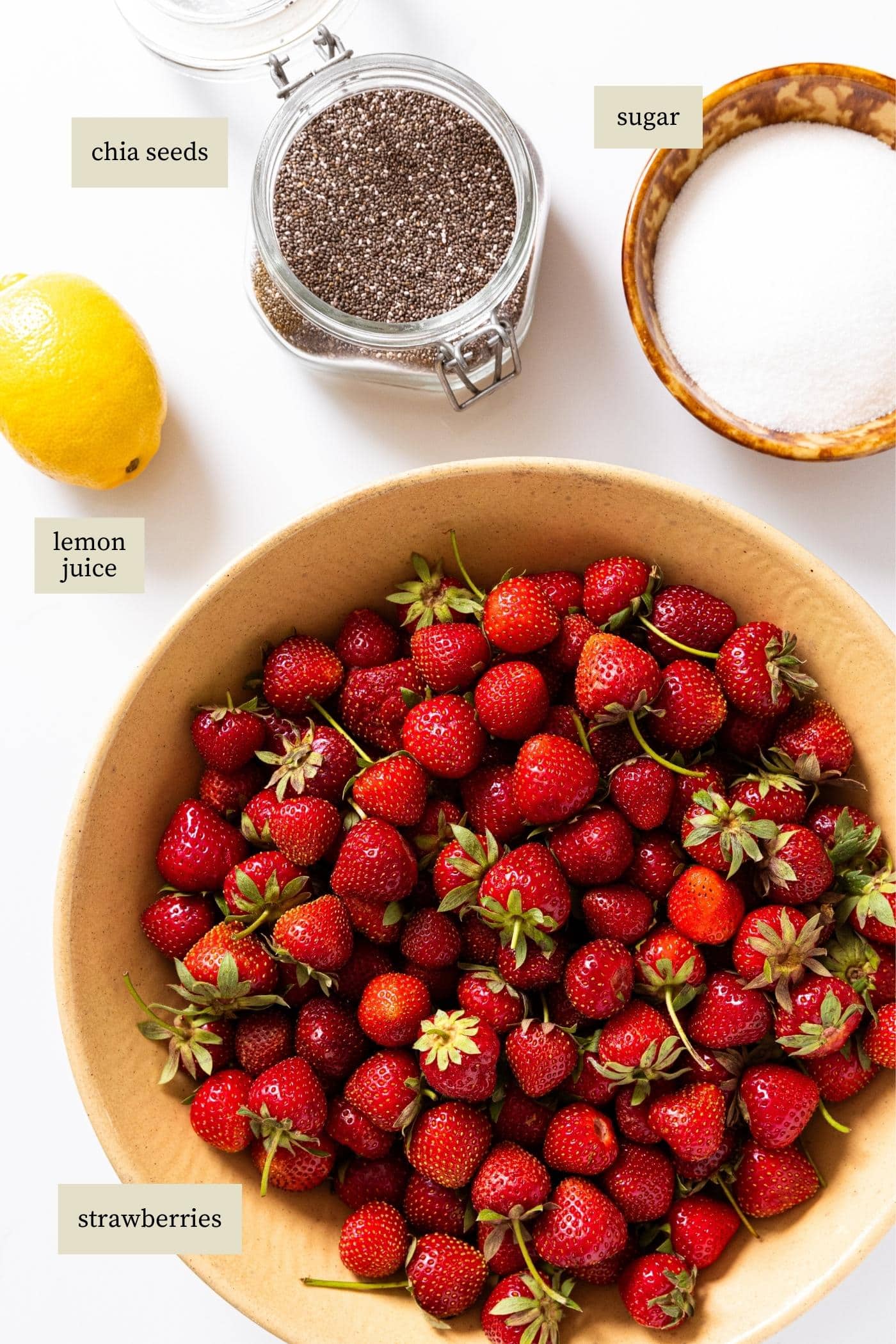 White countertop with bowl of strawberries, whole lemon, chia seeds, and bowl of sugar on top.
