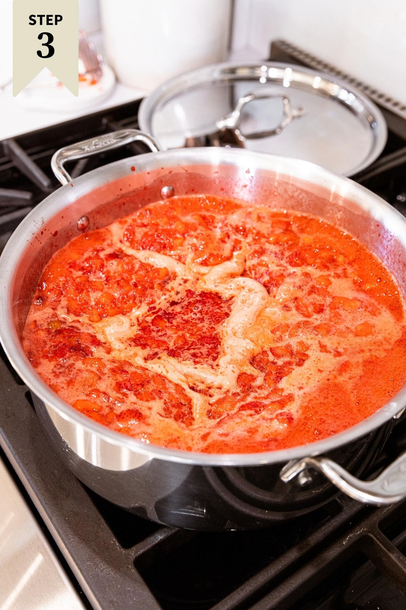 Metal pot filled with bubbling strawberry liquid with foam on top sitting on stovetop.