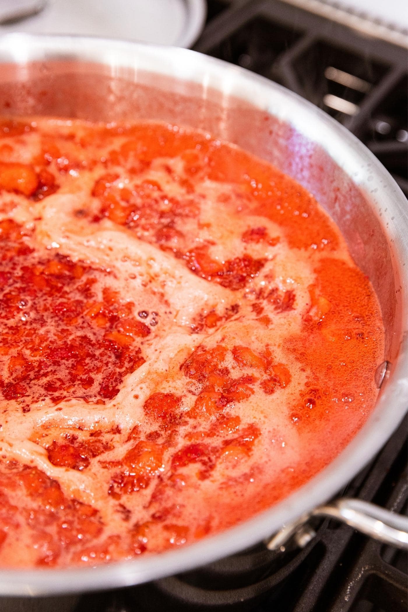 Metal kettle sitting on stovetop filled with bubbling strawberry liquid with foam on top.
