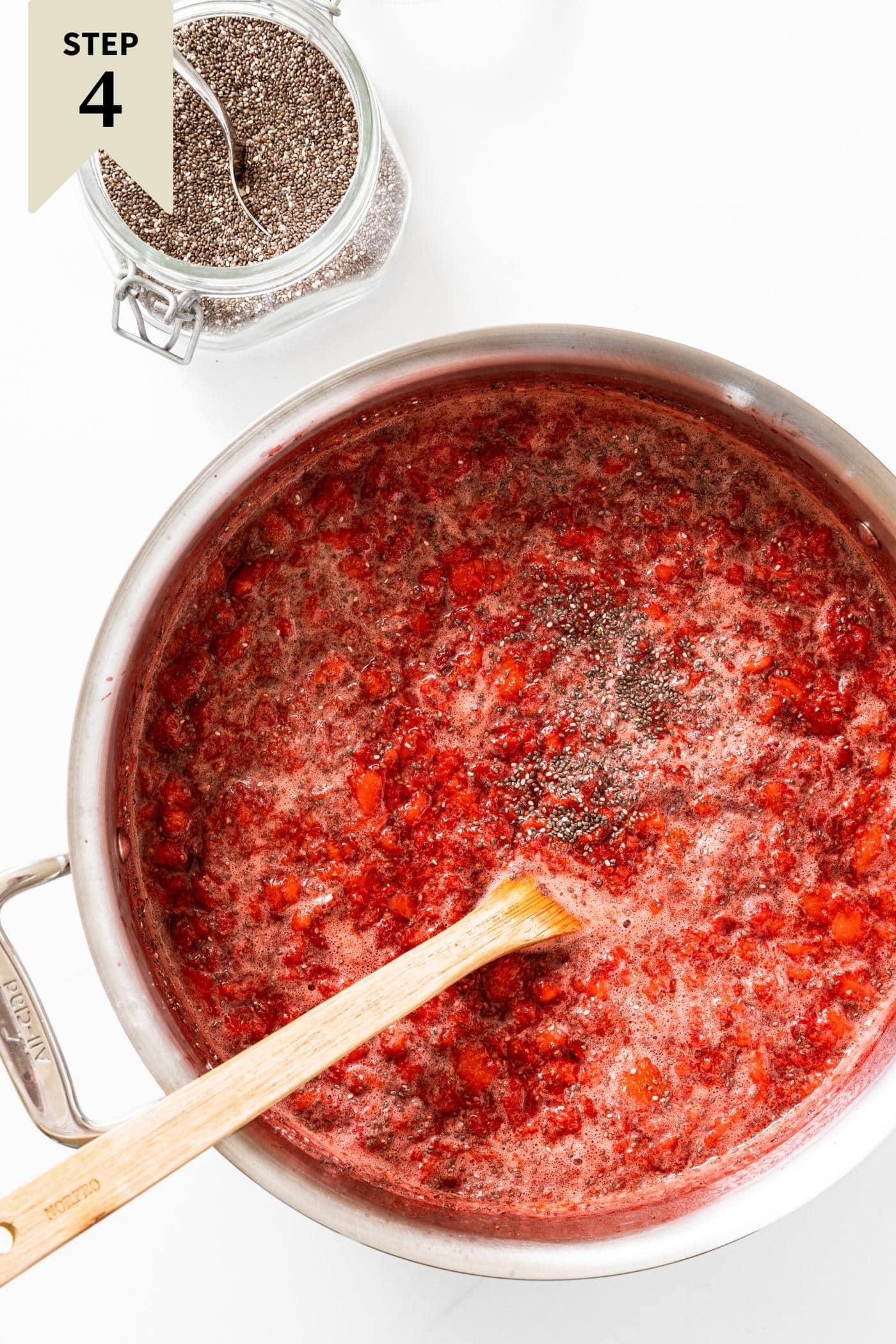 Metal pot filled with strawberry pureé with spoonful of chia seeds sprinkled on top with more chia seeds sitting in container as well.