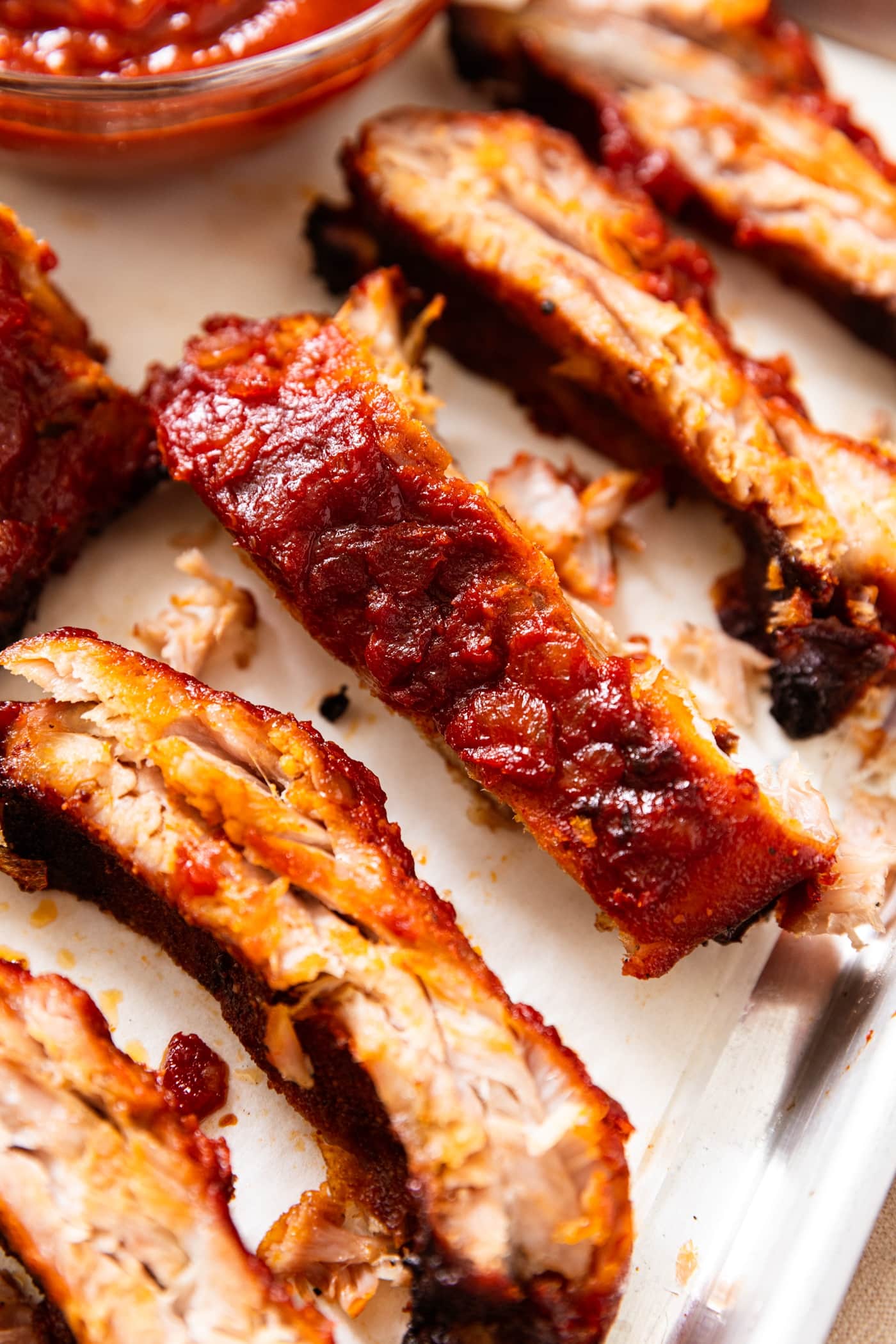 Baby back ribs dripping in sauce sitting on metal baking rack with more sauce to the side.