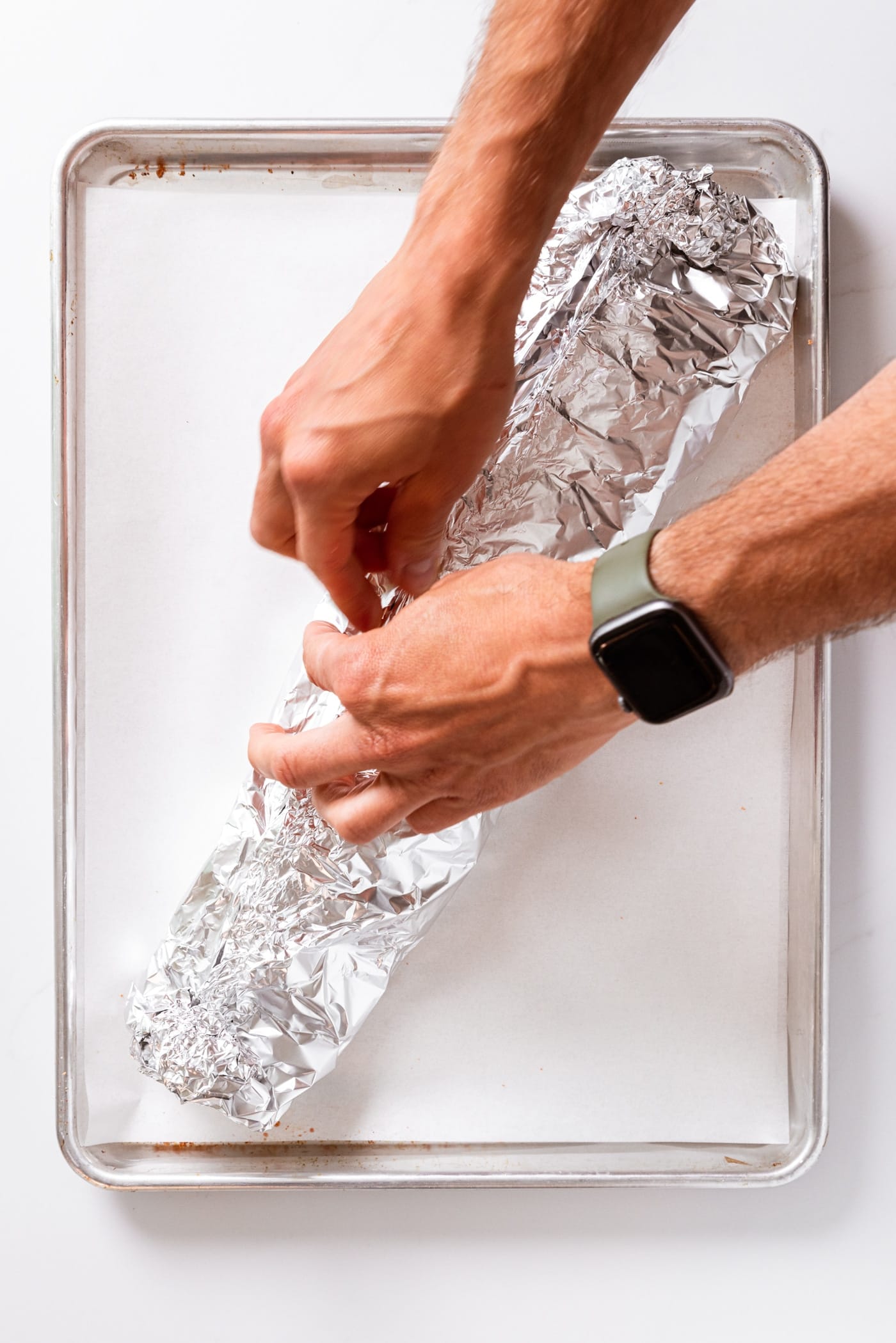 Two hands crimping edges of tin foil together on white countertop.