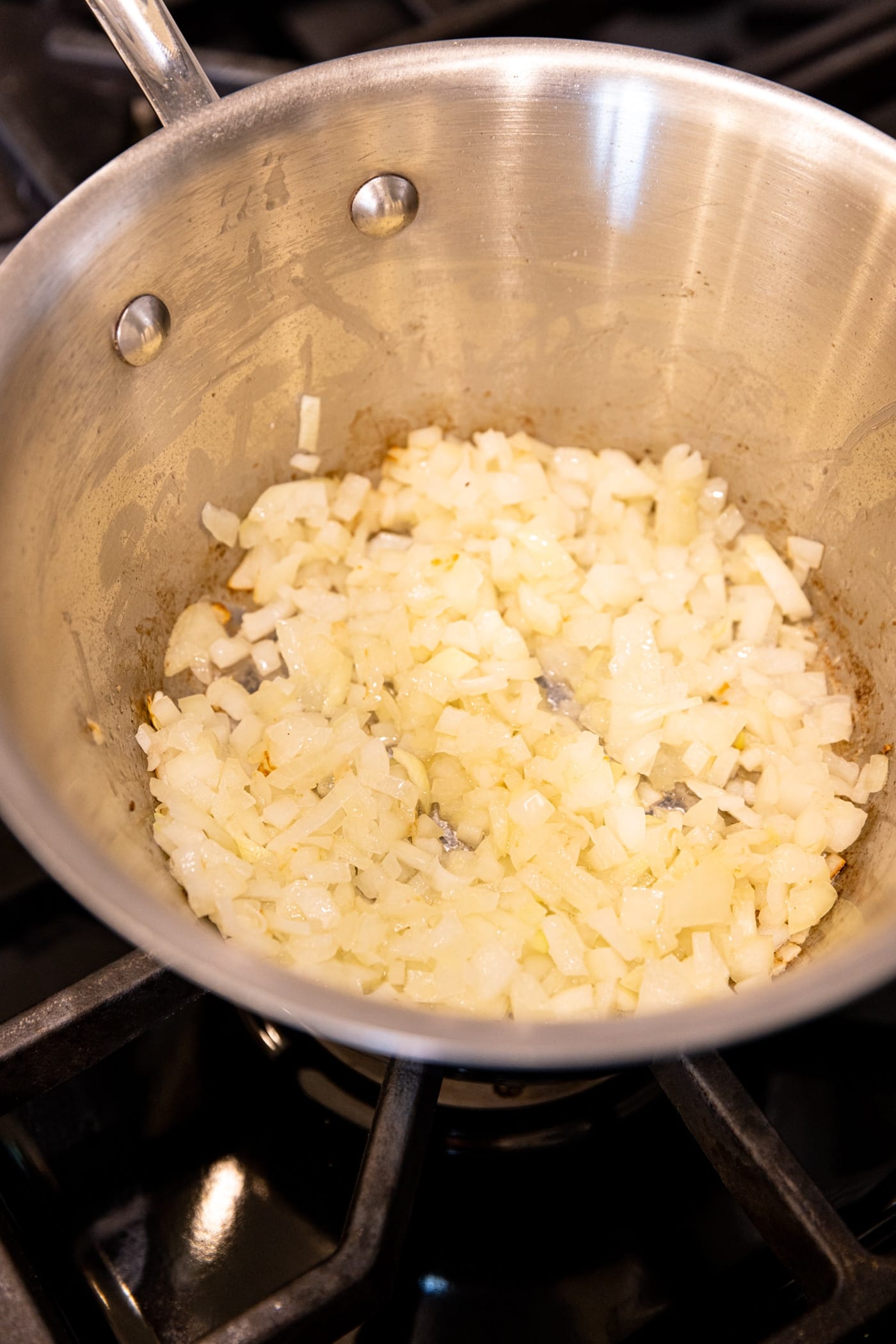 Saucepan sitting on stovetop filled with translucent onion that was sautéed.