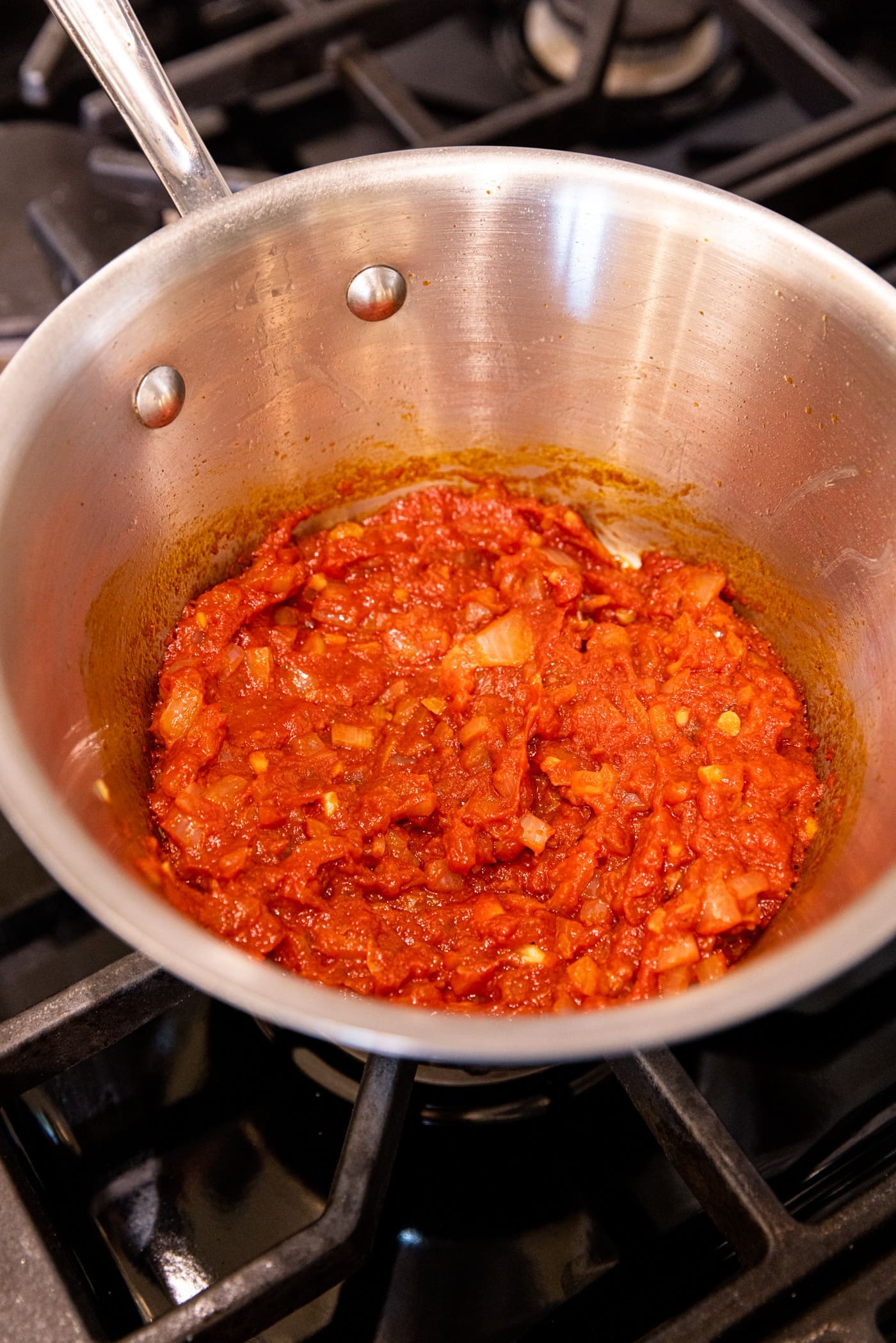 Saucepan holding red sauce with tomato paste freshly poured in.