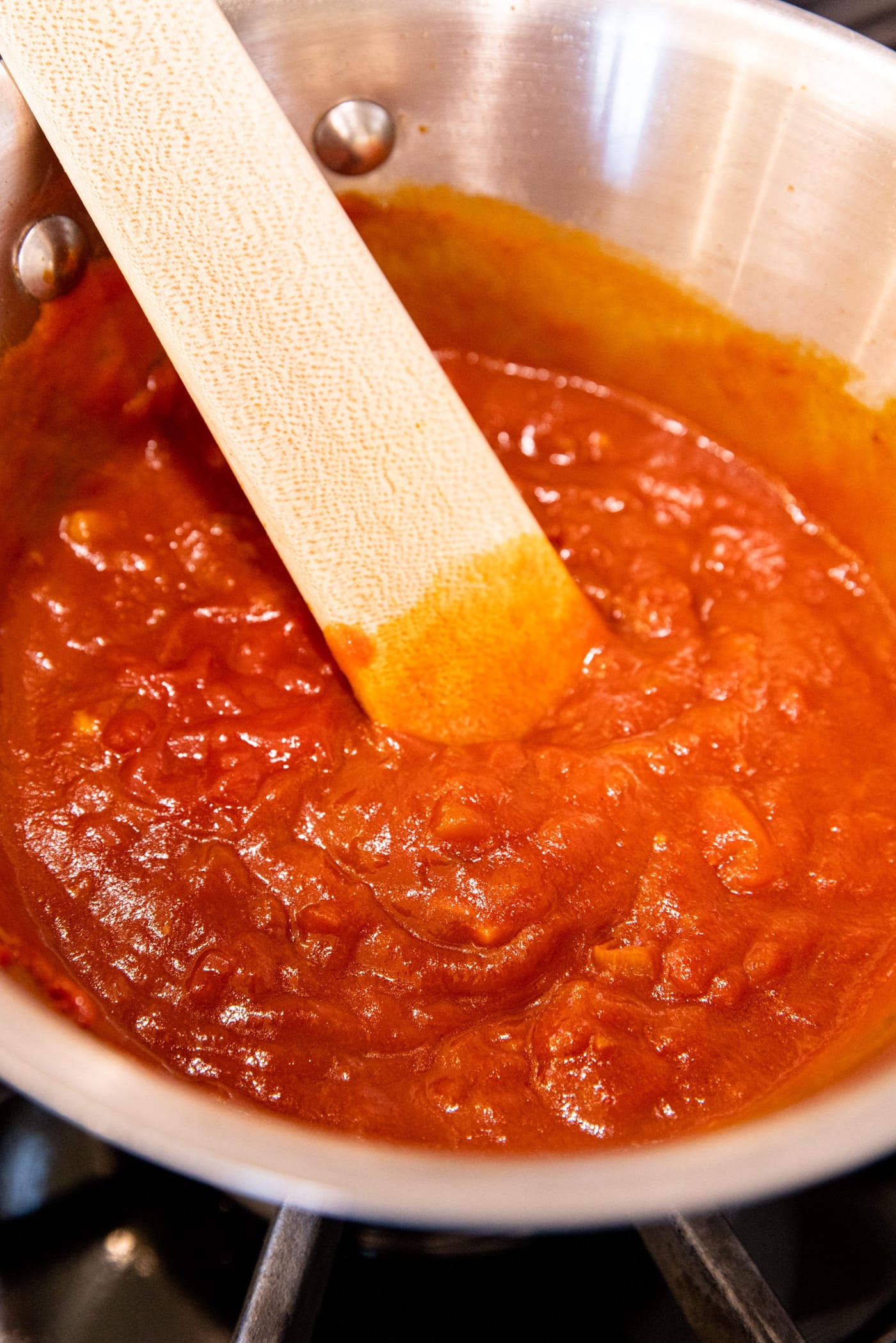 Saucepan with red colored sauce with wooden spatula resting in pan after being stirred.