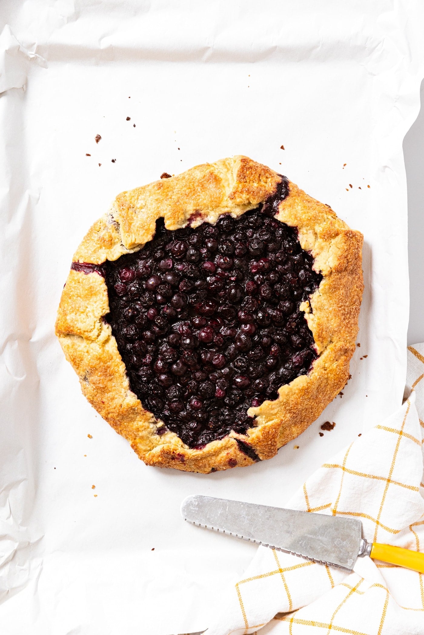 Baked blueberry galette sitting on sheet pan with white parchment underneath.