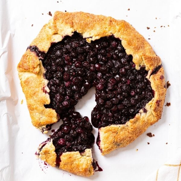 Baking pan with white parchment with baked blueberry galette with one slice pulled out from others.